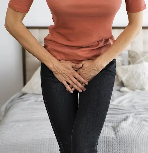 Woman holding lower abdomen for urinary incontinence concern.