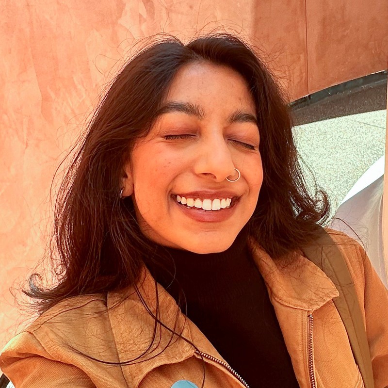 A professional portrait of Manasa Sundaram, a college student from San Jose, CA, showcasing her confident smile and casual attire. She is seen against a neutral background, reflecting a vibrant and approachable personality.