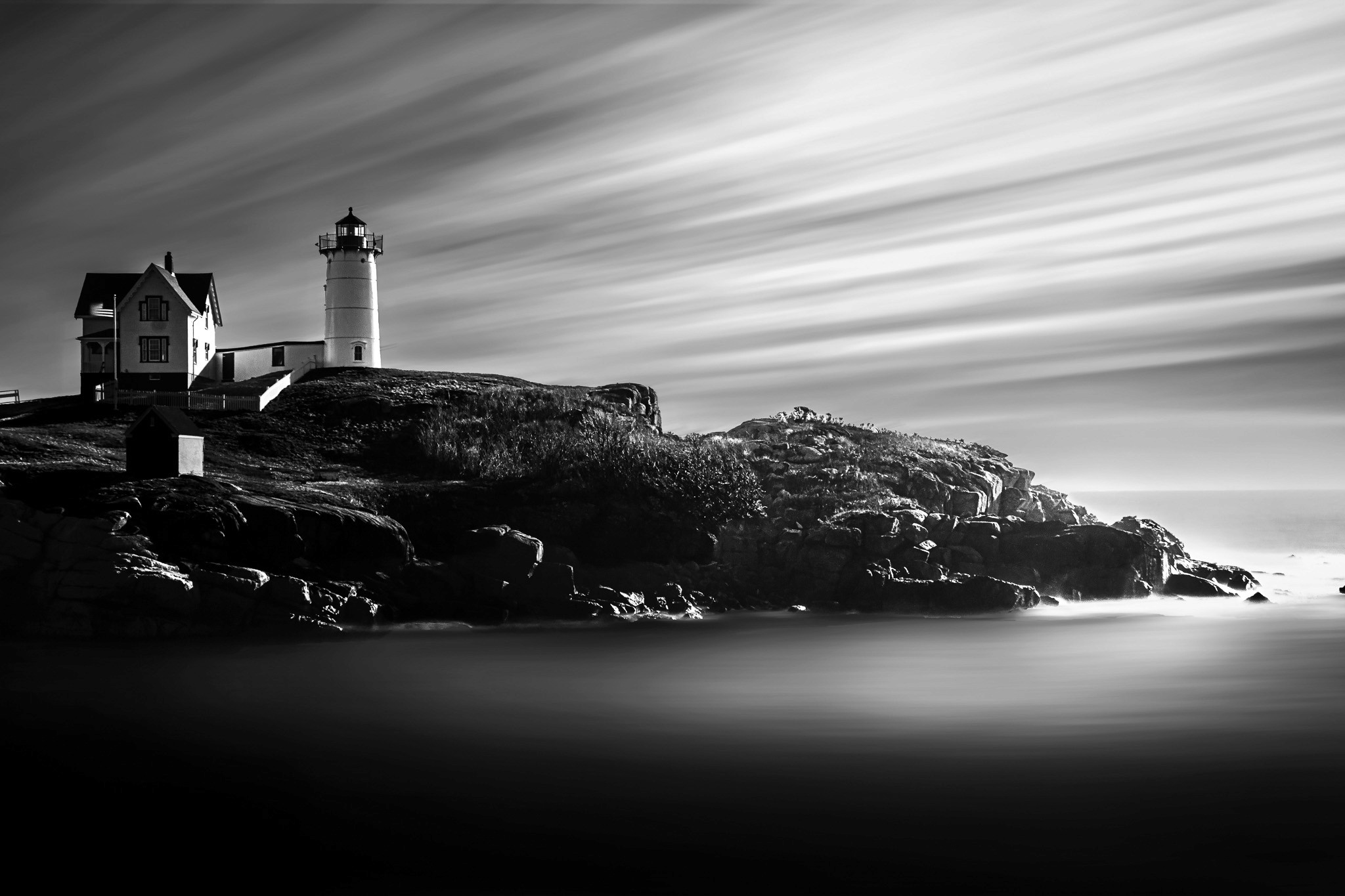 A man standing on a leaf-covered rock looking up at the rock formation above with a waterfall in the background