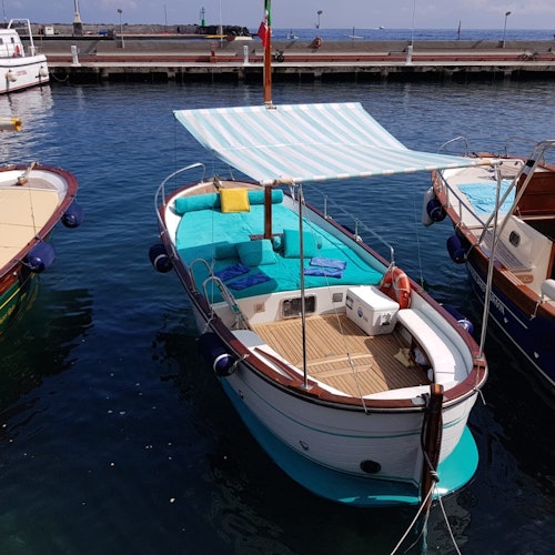 Small boat with turquoise cushions and a striped canopy docked at a marina, flanked by other boats.