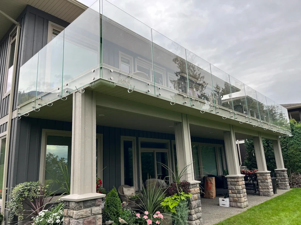 Contemporary two-storey home with frameless balcony glass railing supported by stone pillars, enhancing open architectural design.