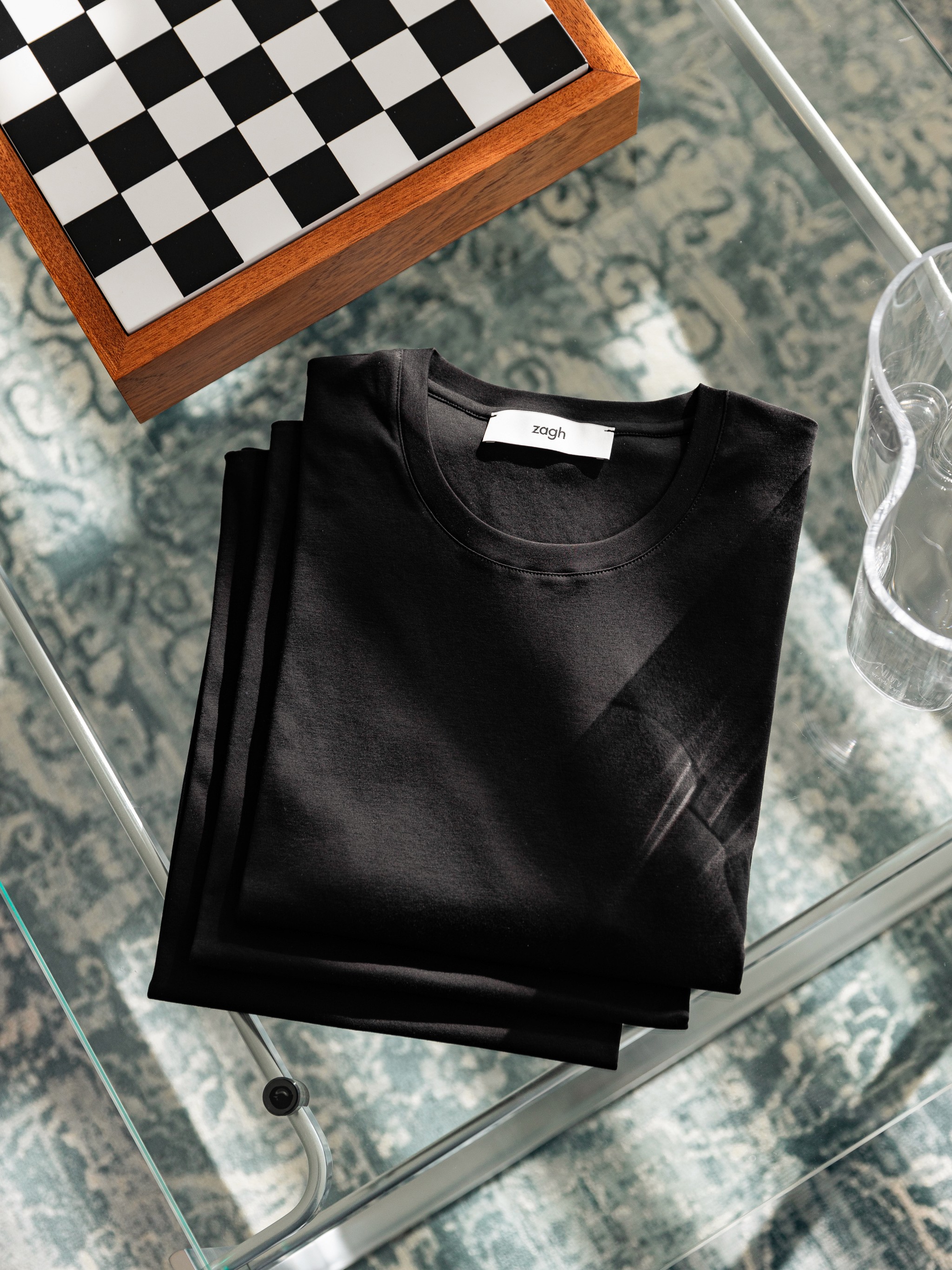 Flat-lay of a black cotton ZAGH shirt beside a chessboard — tactile, masculine, refined.