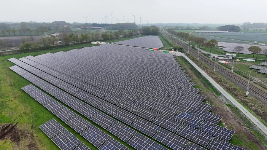 Großes Solarkraftwerk mit Reihen von Photovoltaikmodulen und Windrädern am Horizont.
