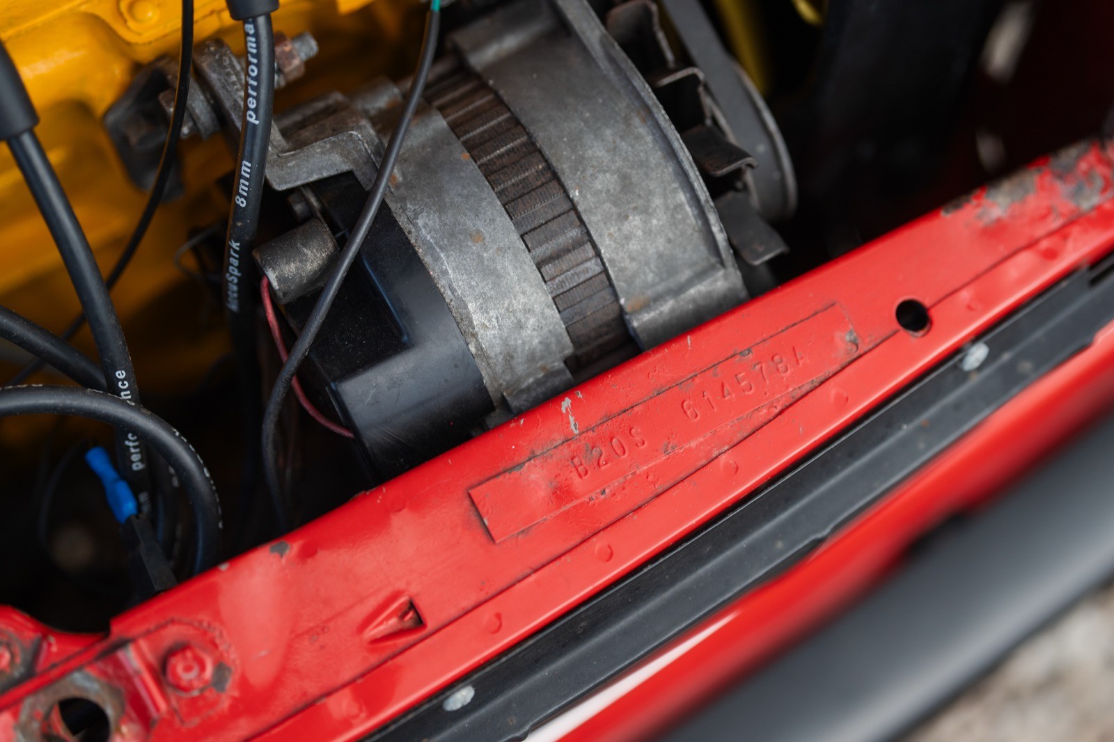 Close-up of a car engine bay featuring a red component with visible wiring and other mechanical parts.