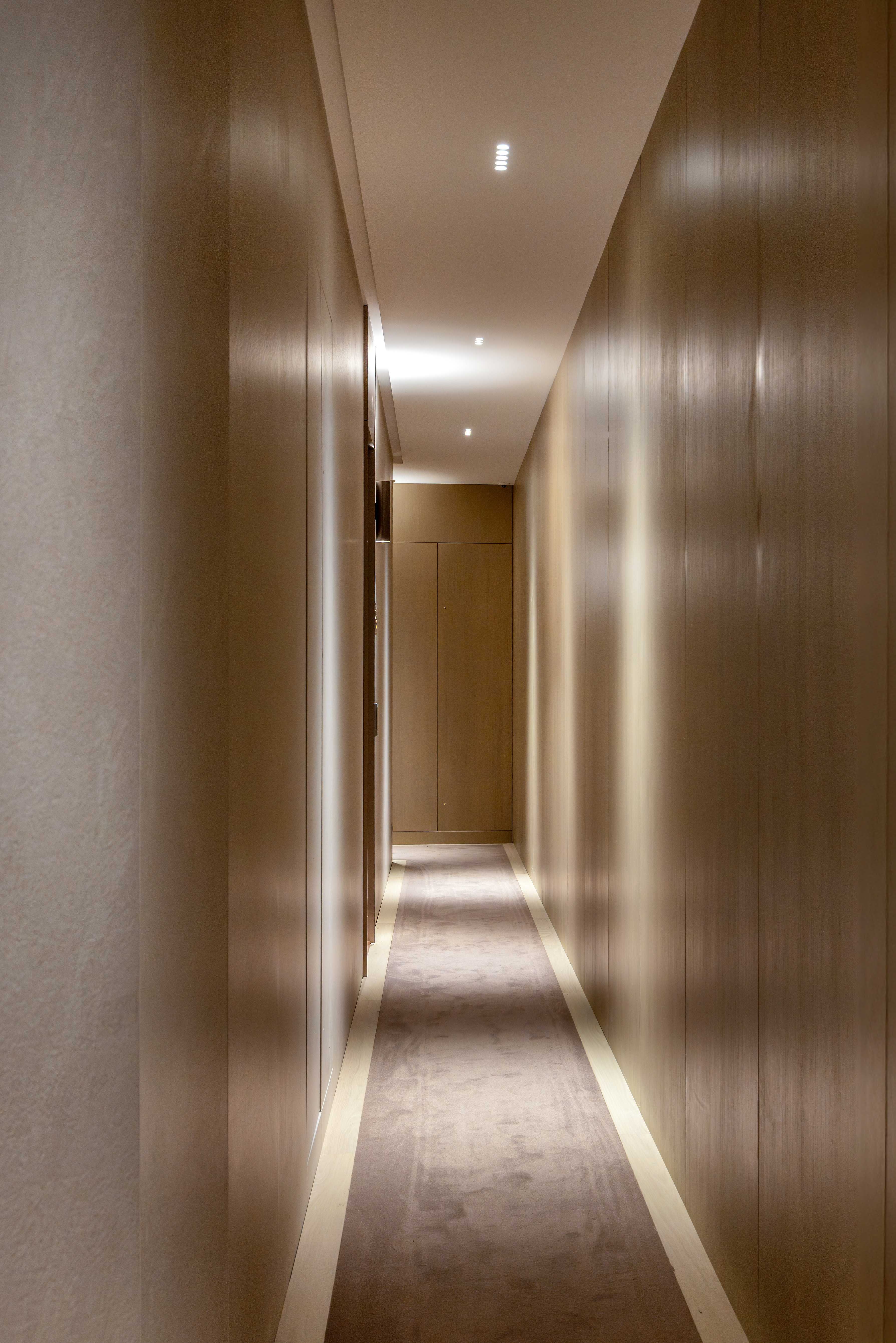 Couloir d'étage en bois clair avec moquette beige, spots encastrés et éclairage linéaire au sol