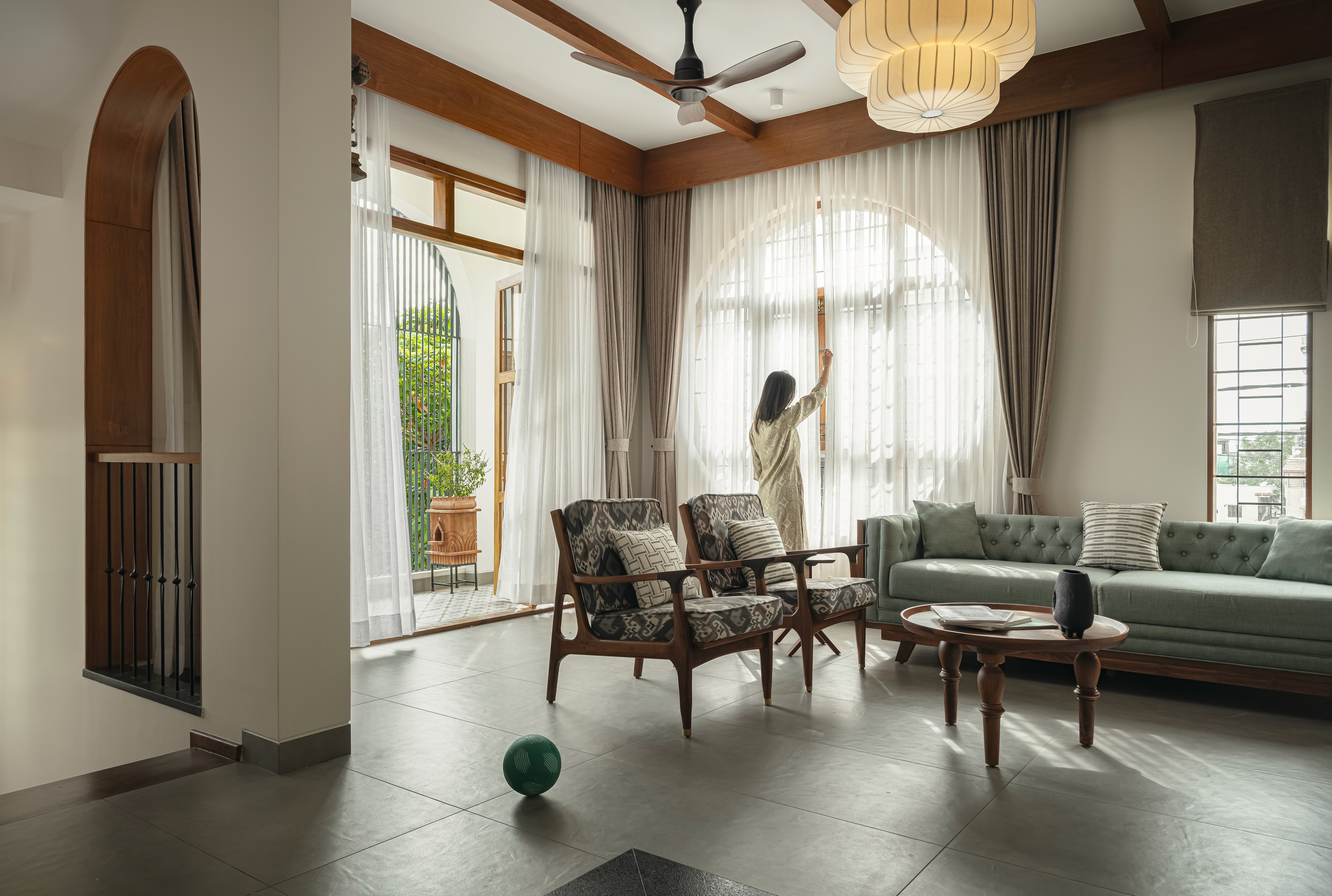 Sunlight streaming through lush green trees, casting shadows on a modern architectural building with glass panels and vertical wooden slats.