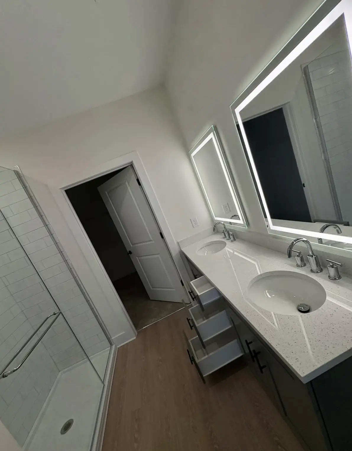 A sanitized master bathroom after a move-out cleaning, featuring open vanity drawers to show clean interiors, polished chrome faucets, and a sparkling glass shower.