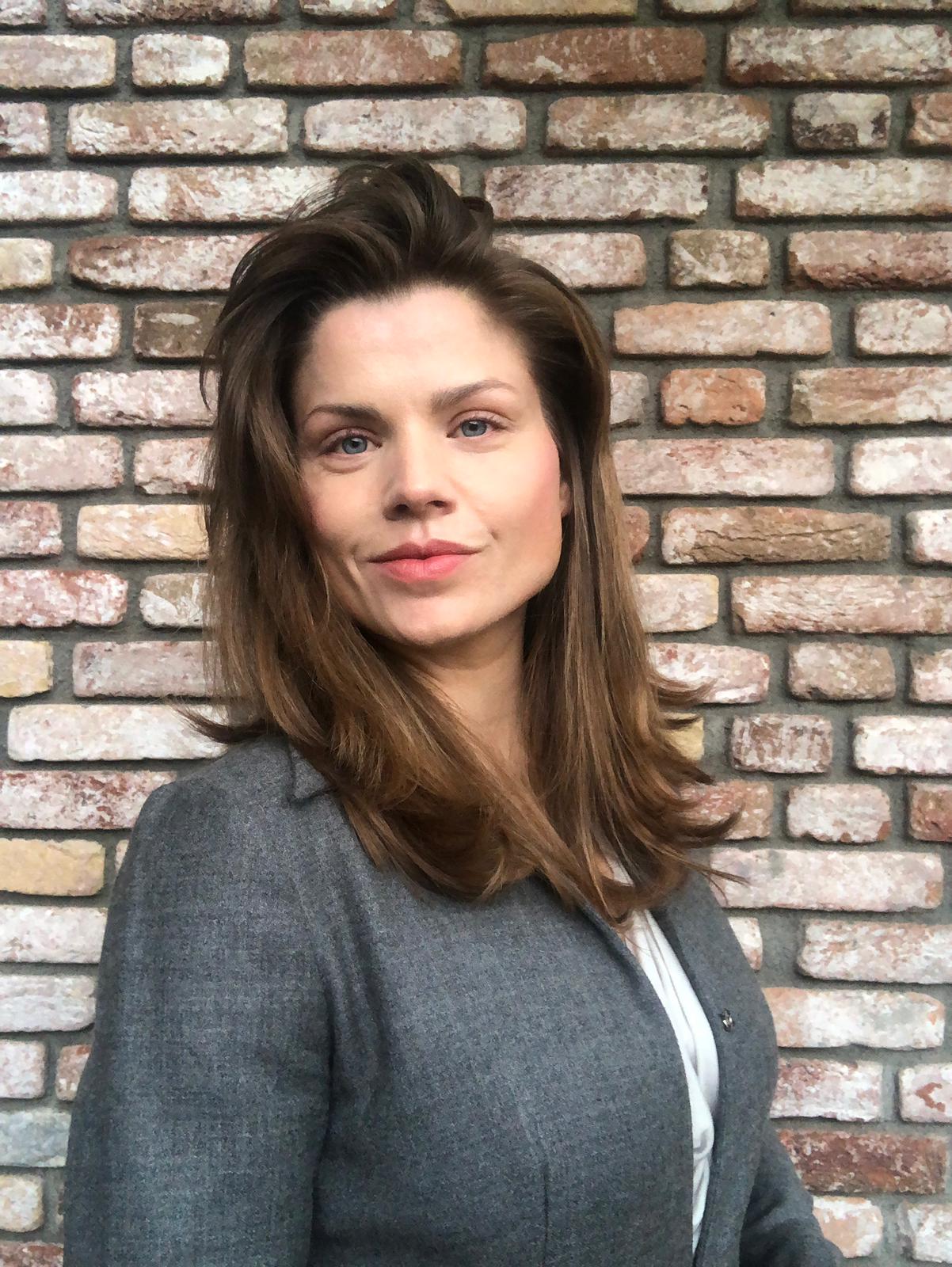 Tosca de Jong, EU/NATO-scale systems thinker and governance writer, in a grey blazer against a brick wall, confident professional portrait.
