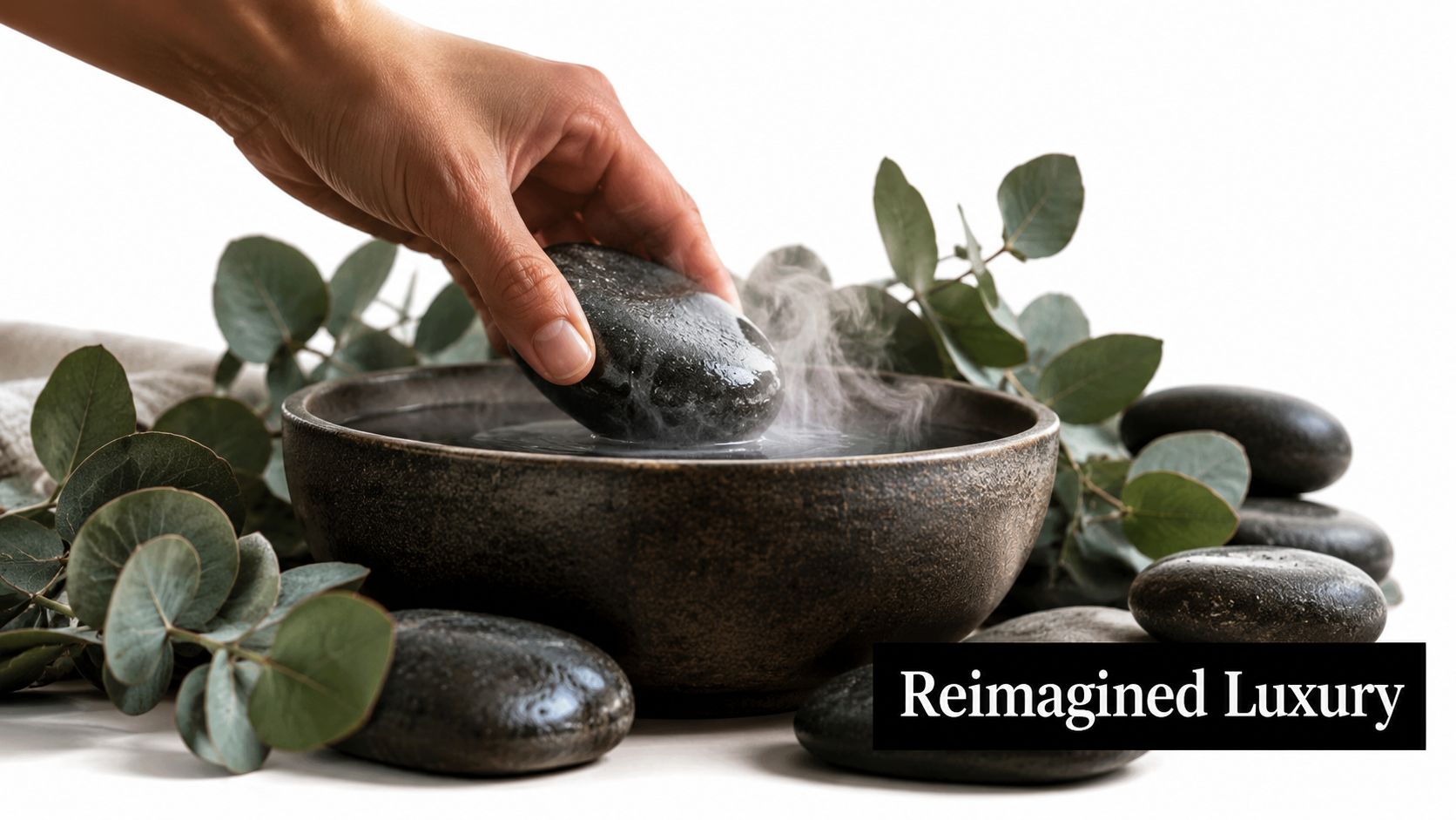 A hand placing a steaming hot black spa stone into a ceramic bowl of water with eucalyptus.