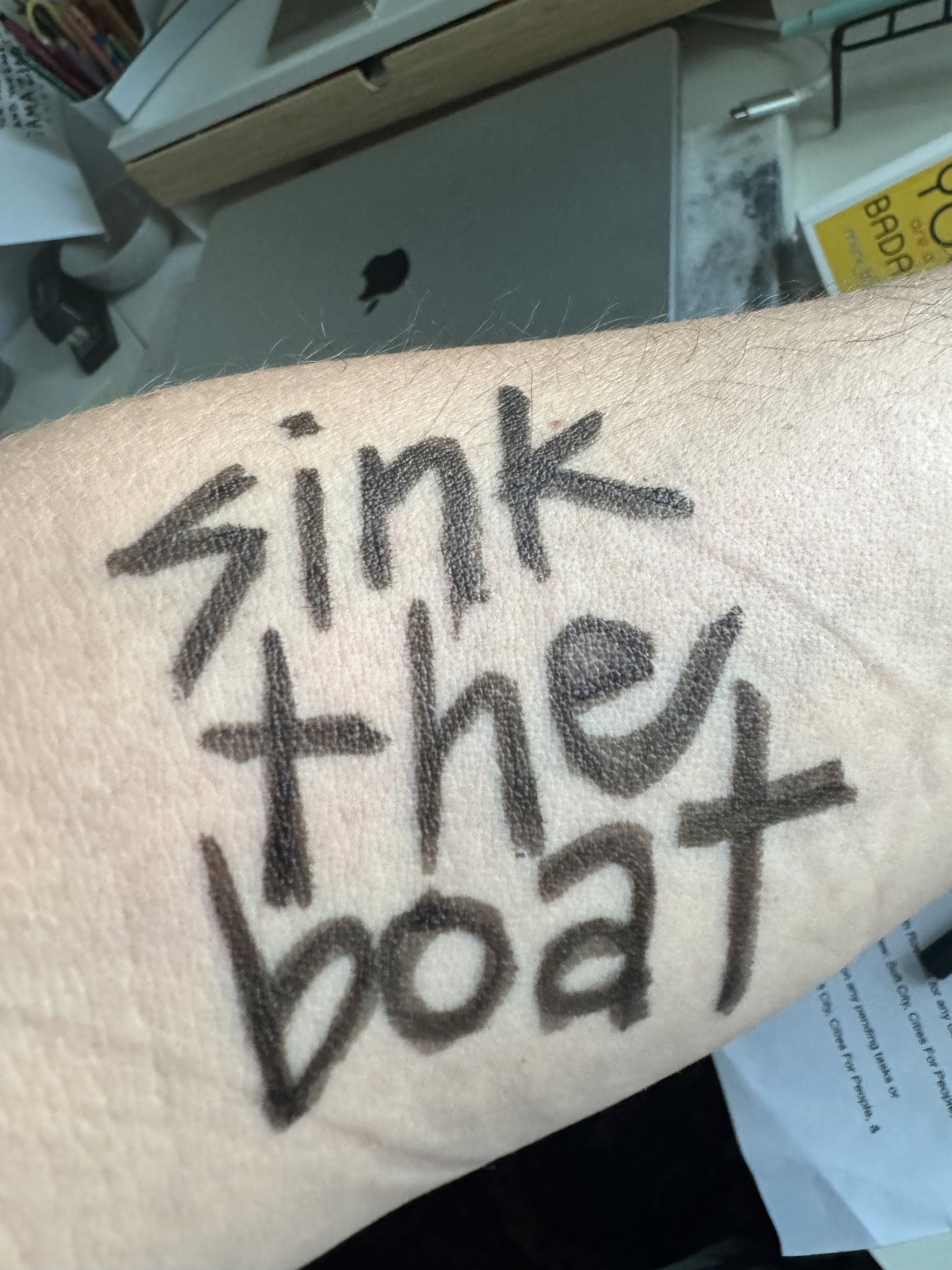 A handdrawn tattoo on a forearm that reads sink the boat, photo by Rafia Mahli.