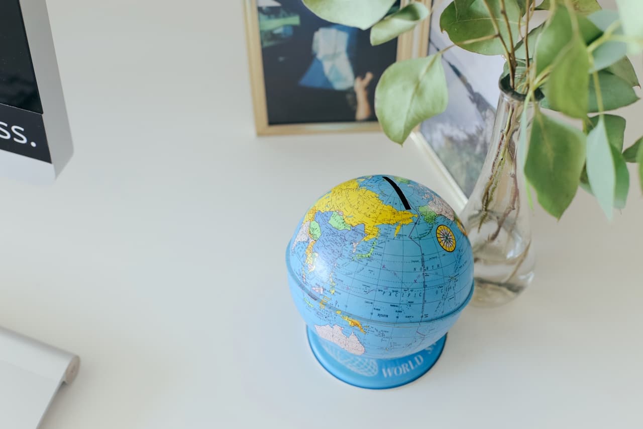 A small globe on a desk near a vase with leaves and a photo frame