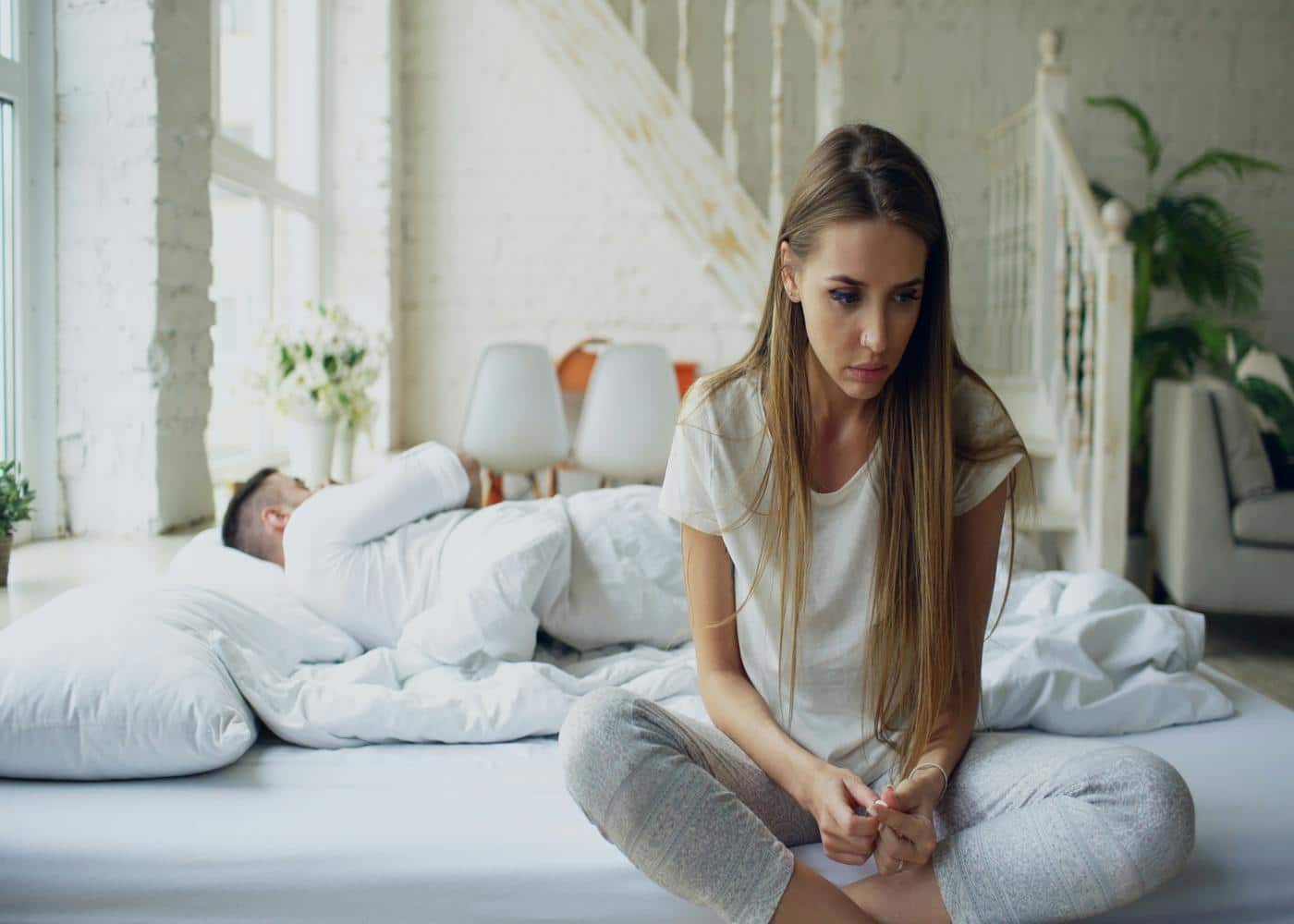 Causes of low libido - woman sitting on edge of a bed and man lying with backs to each other