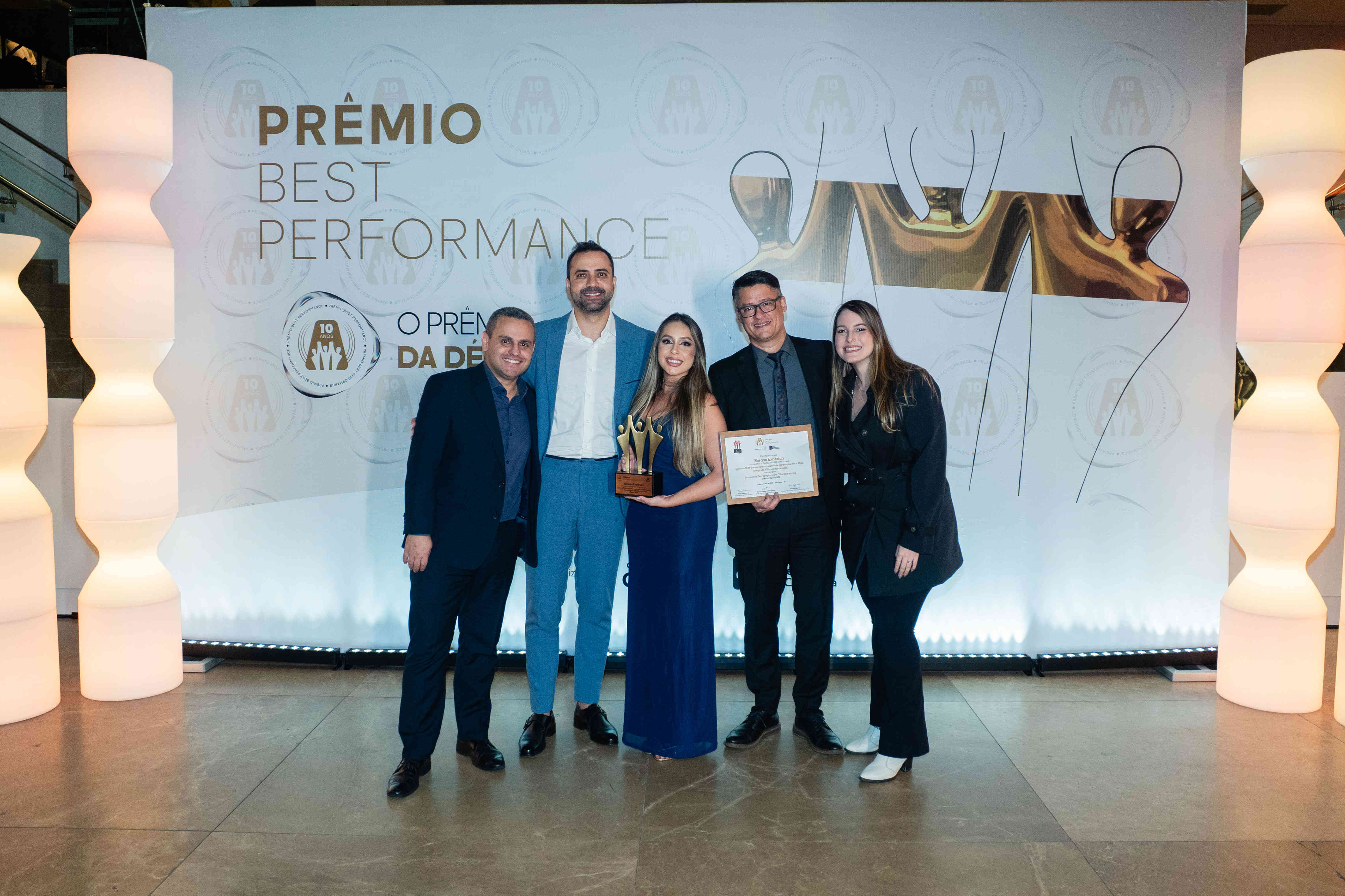 Executivos da Serasa Experian posando com troféu bronze e certificado no palco do Prêmio Best Performance 2025.