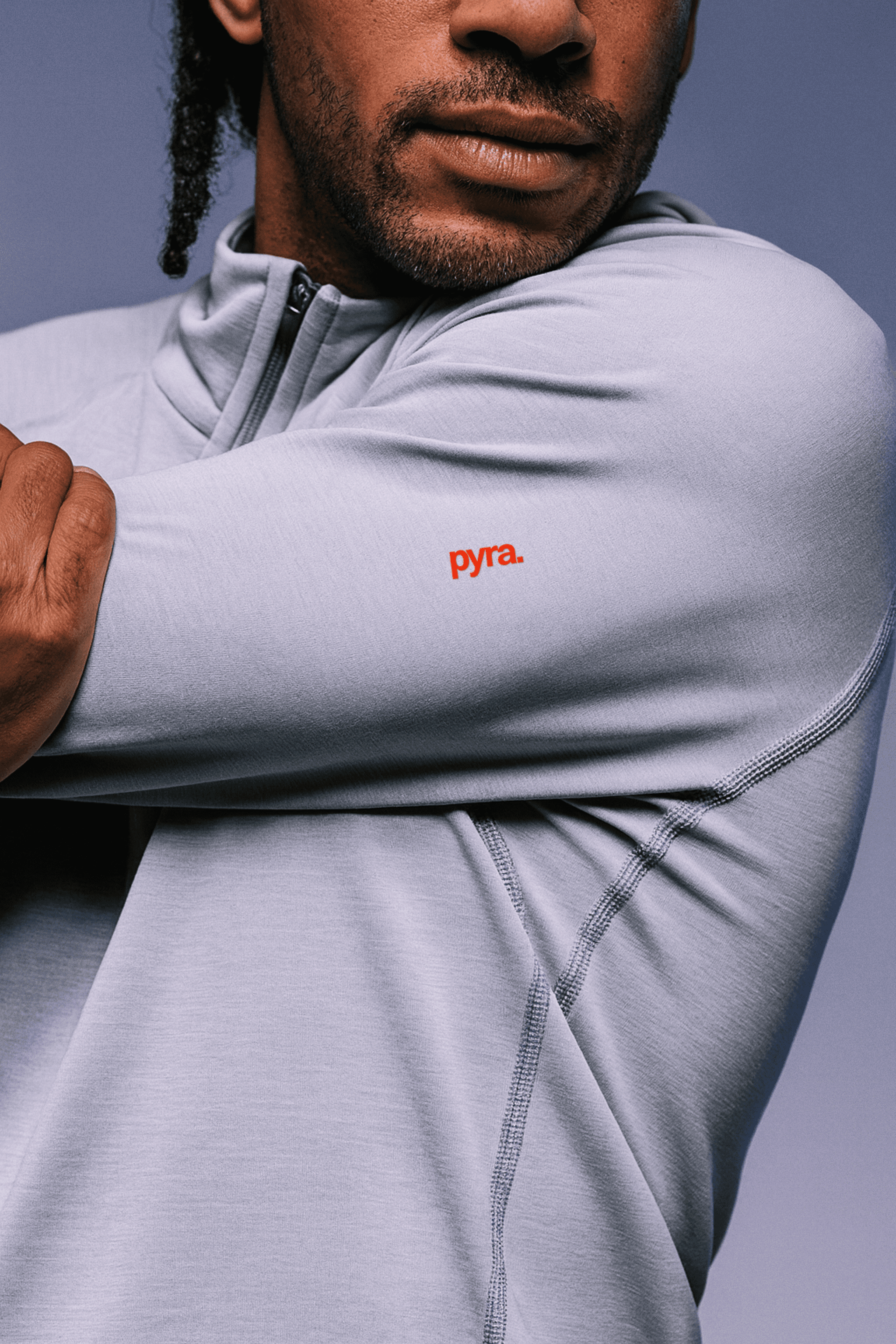 Close-up of a man stretching in a light gray athletic top with a red "pyra." logo on the sleeve.