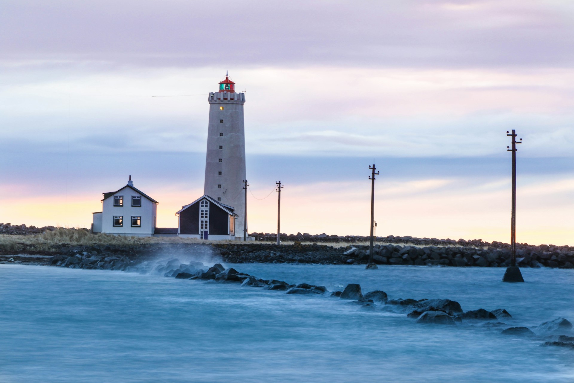 Grótta Lighthouse on the Seltjarnarnes Peninsula with calm coastal waters at sunset.