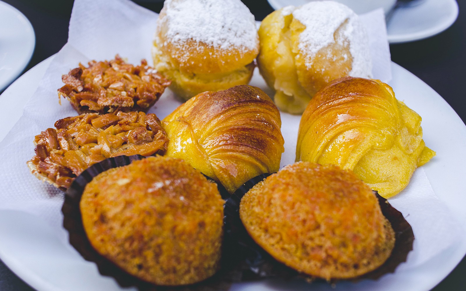 葡萄牙糕點,包括杏仁撻和撒糖的捲餅,擺放在盤子上。