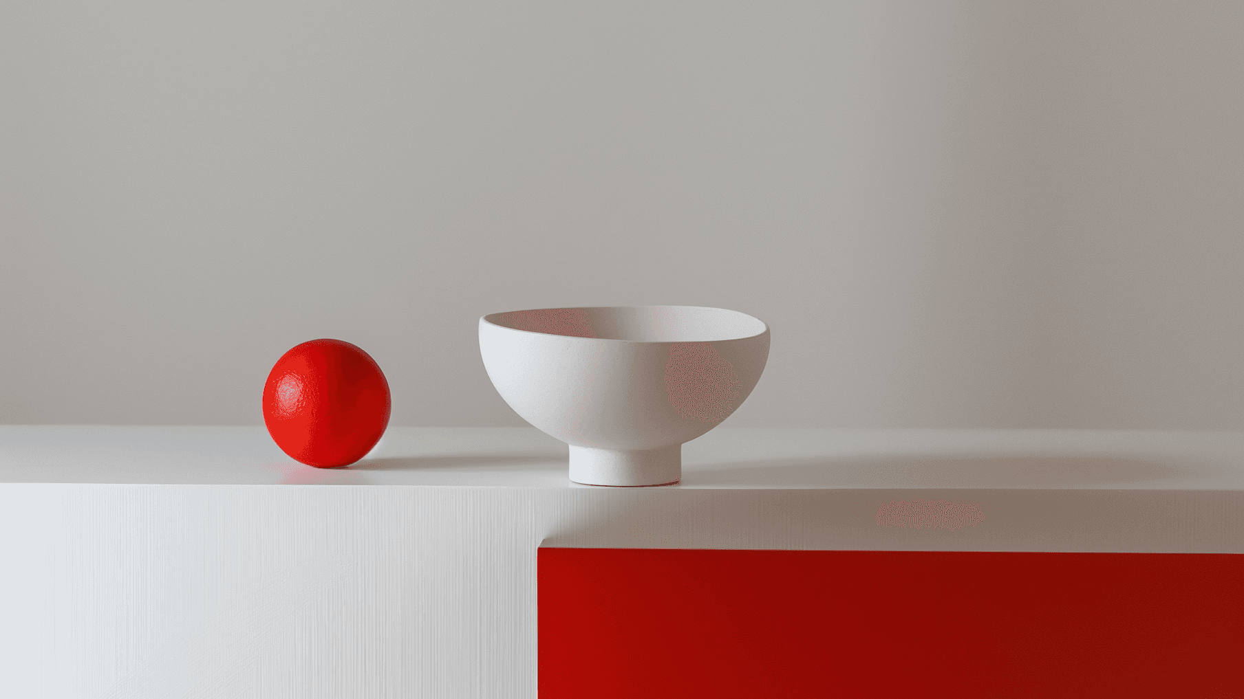 Minimalist scene with a red sphere and white bowl on a two-tone surface, blending modern design and color contrast.