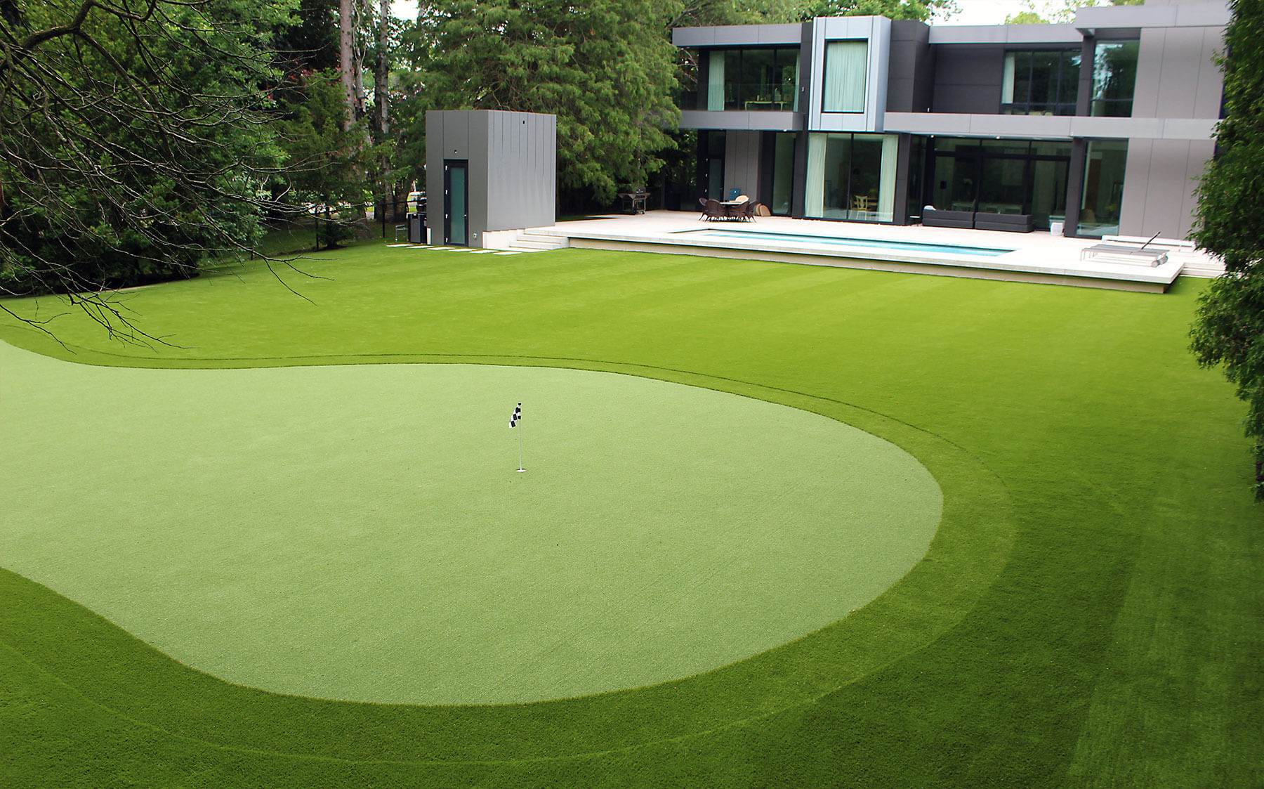 Lush AGL Grass artificial turf covers the backyard of a sleek, modern house, creating a vibrant outdoor space for chipping, putting, and relaxing.