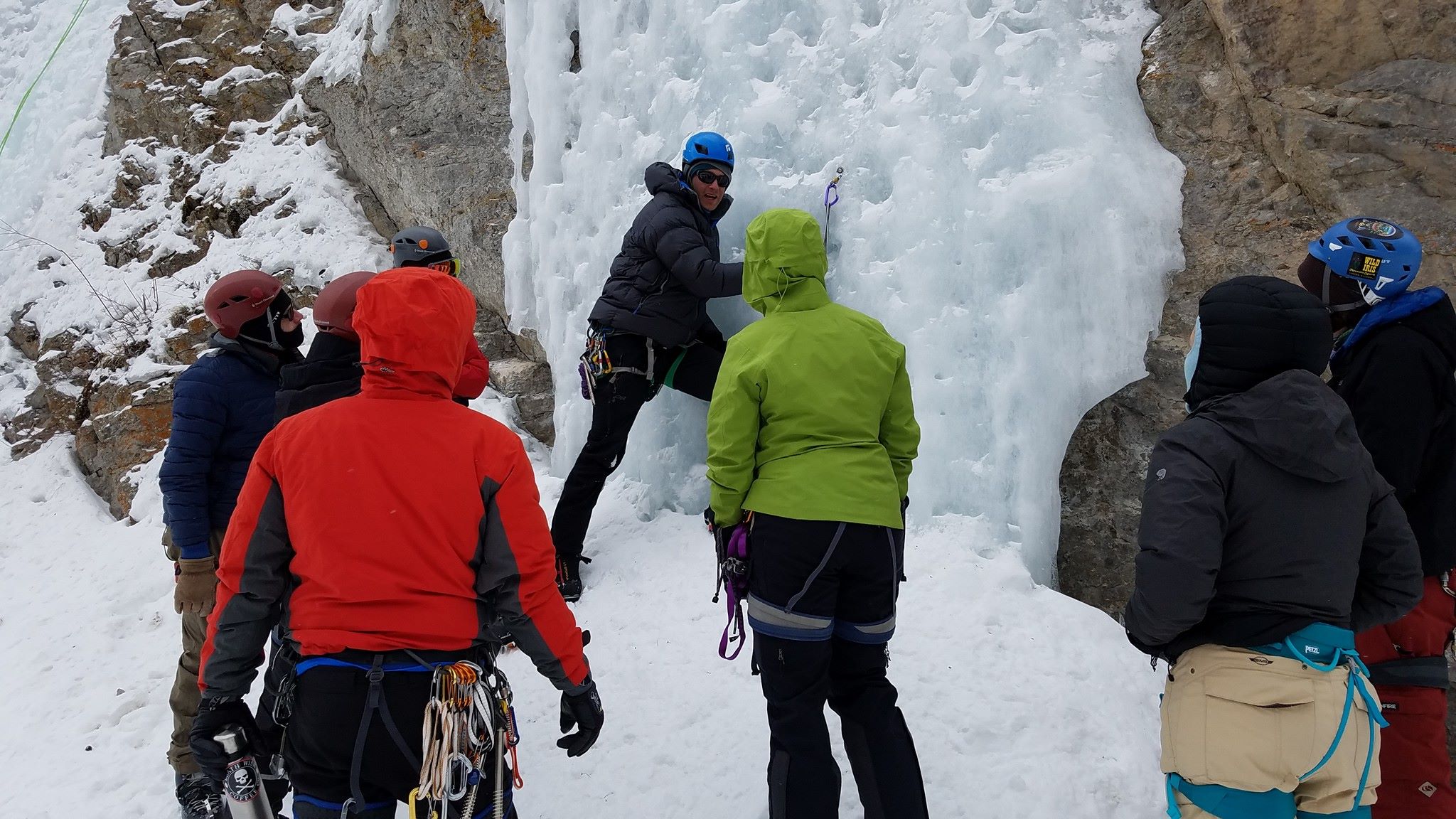 New ice climbers surround guide at the base of ice route as they explain ice climbing techniques