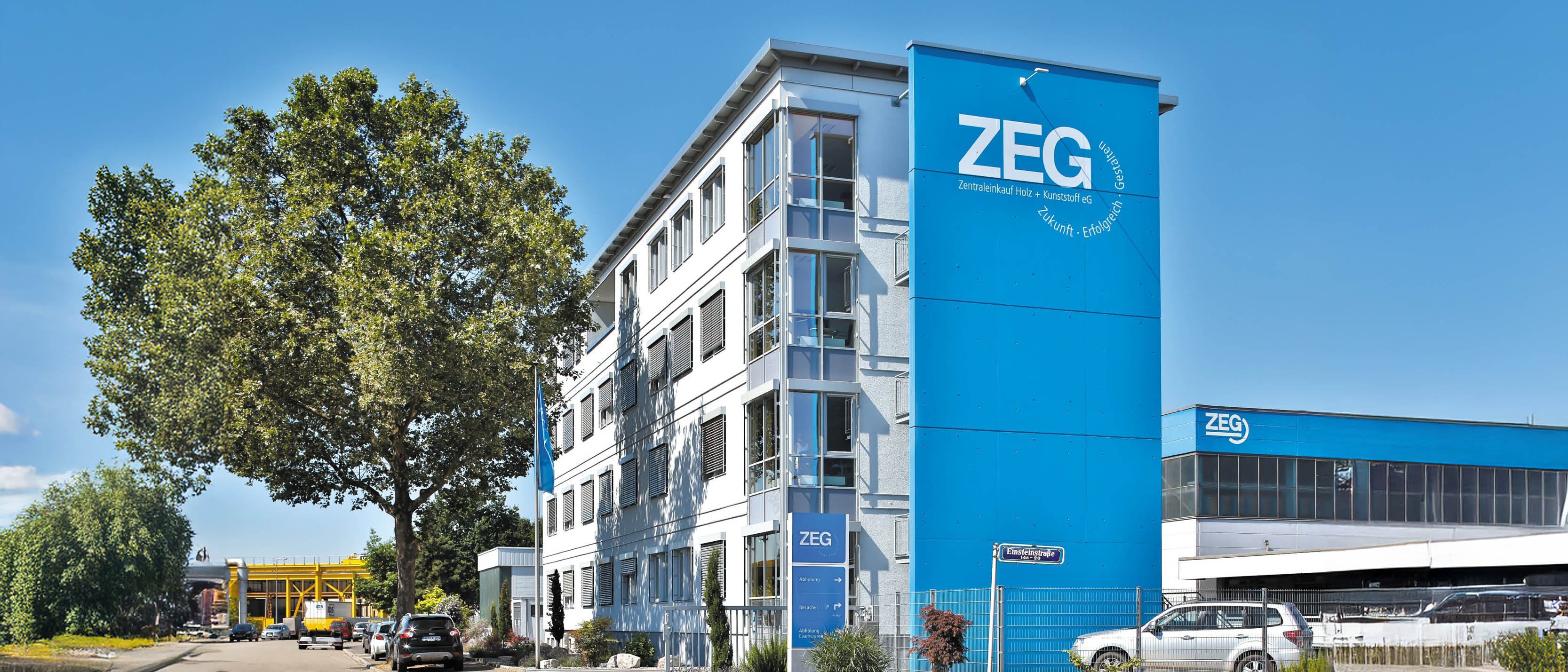 Modernes Bürogebäude der ZEG mit großem, blauem Schriftzug und Werbeslogan vor strahlend blauem Himmel.