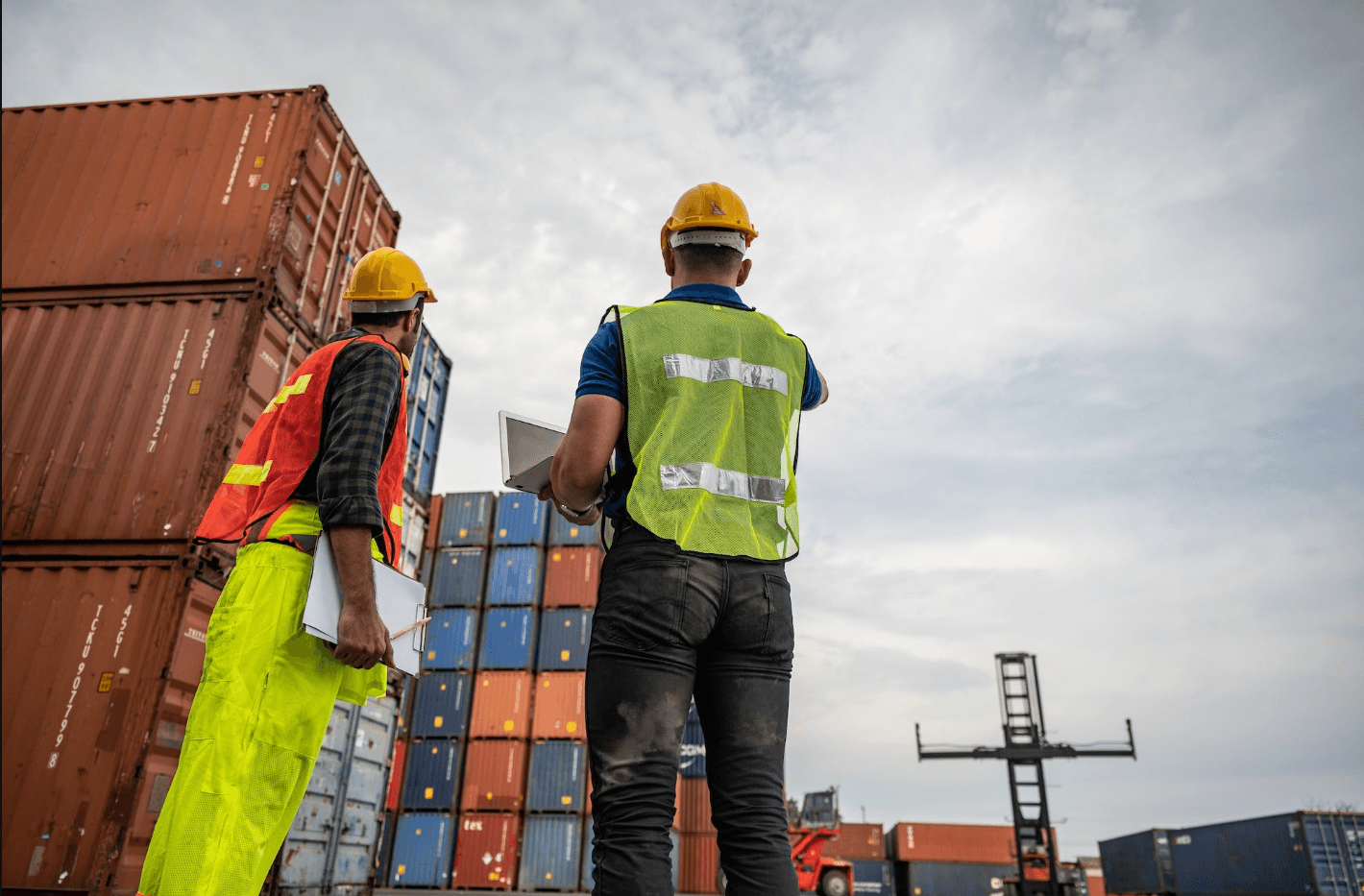two men wearing high vis looking at shipping containers