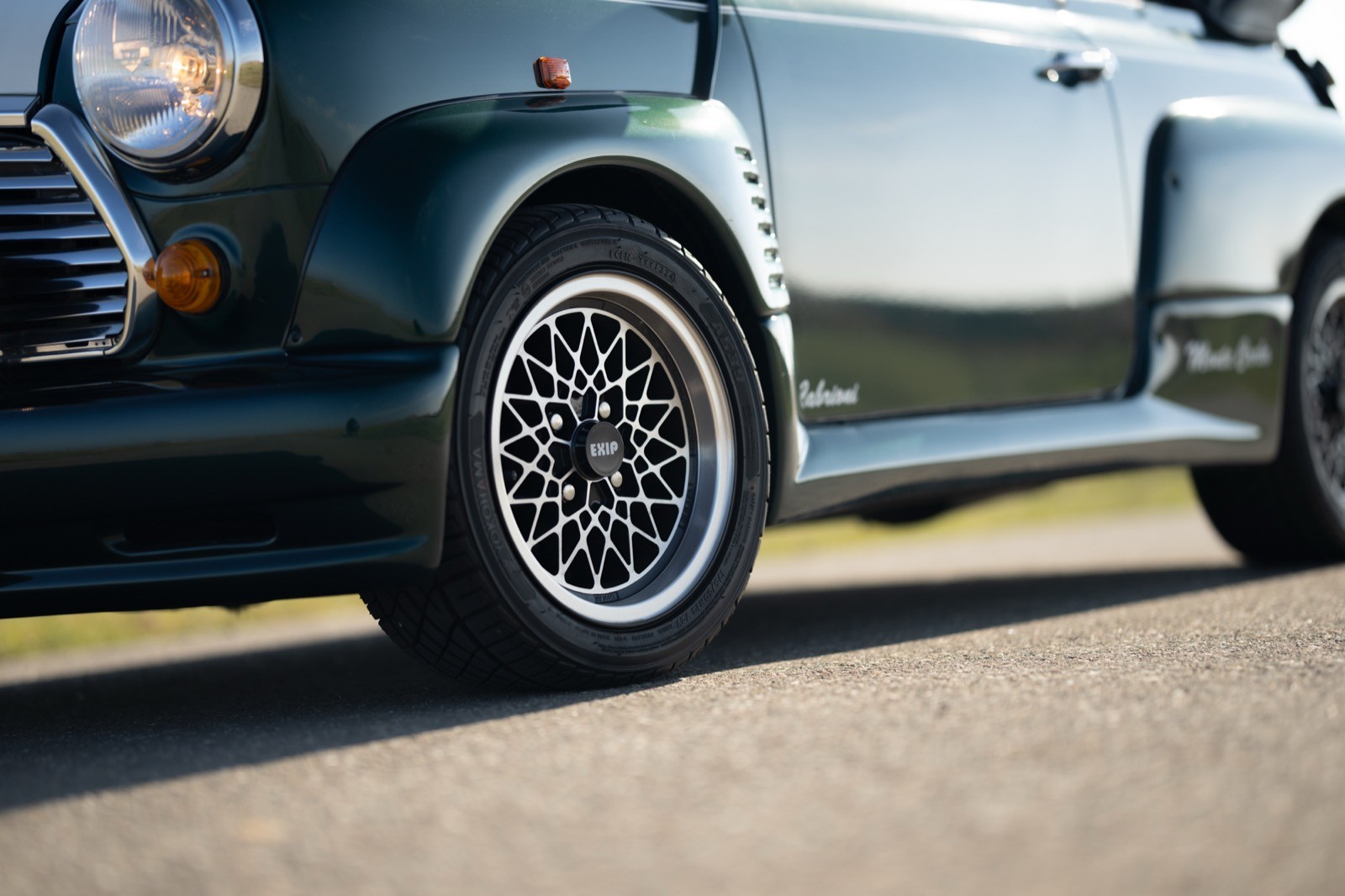 Close-up of a car's wheel and tire on a paved road with a blurred background, showcasing detail and design.