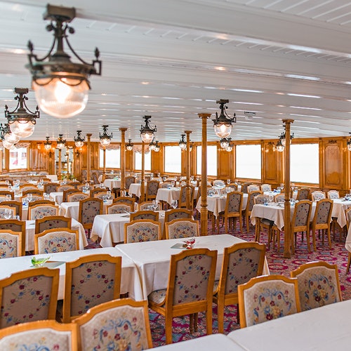 一間光線明亮、裝飾華麗的餐廳,配有花卉圖案的椅子、白色桌布和復古的吊燈。