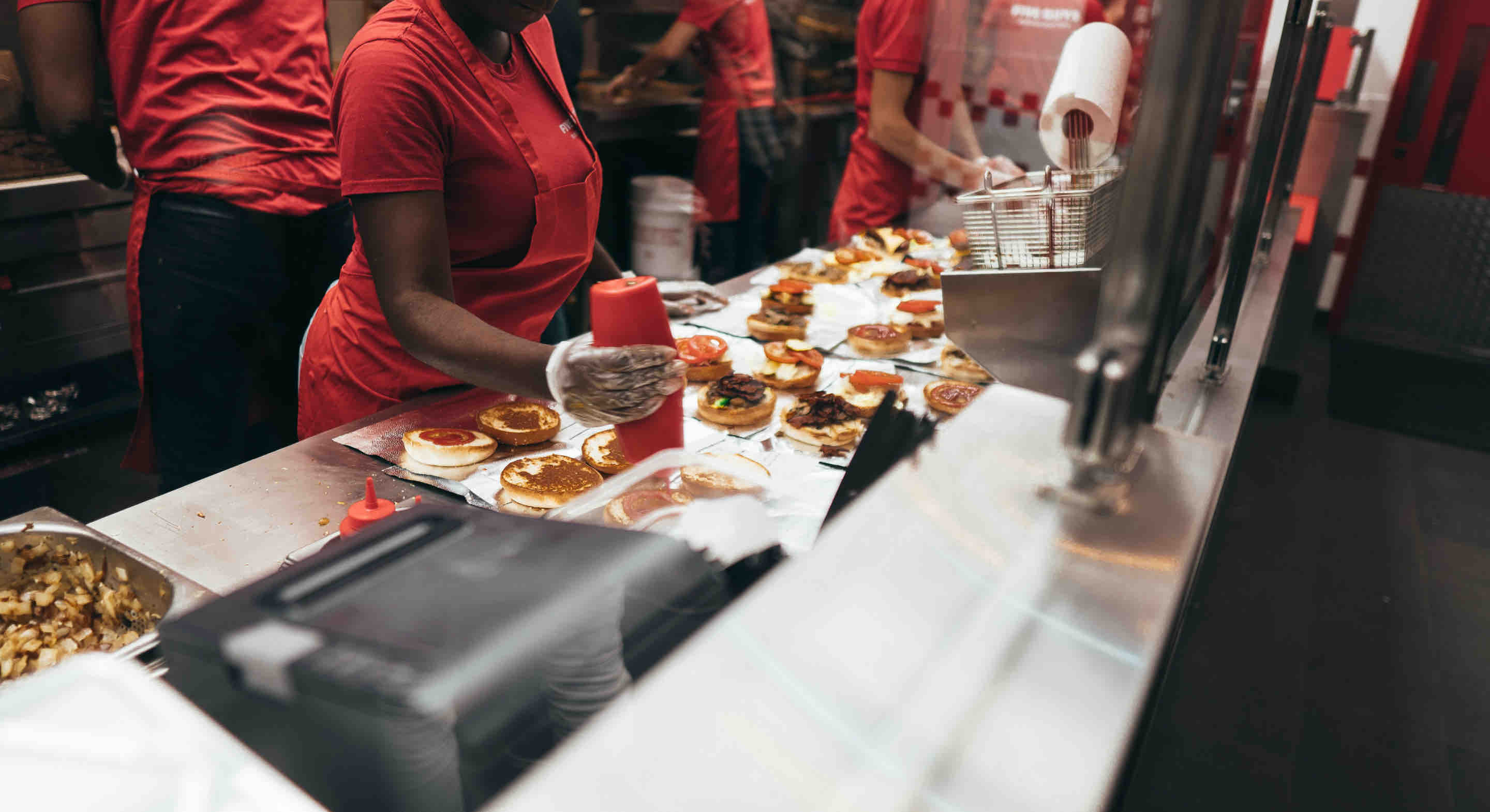 Photo of a person preparing cheeseburgers in a fast food restaurant.