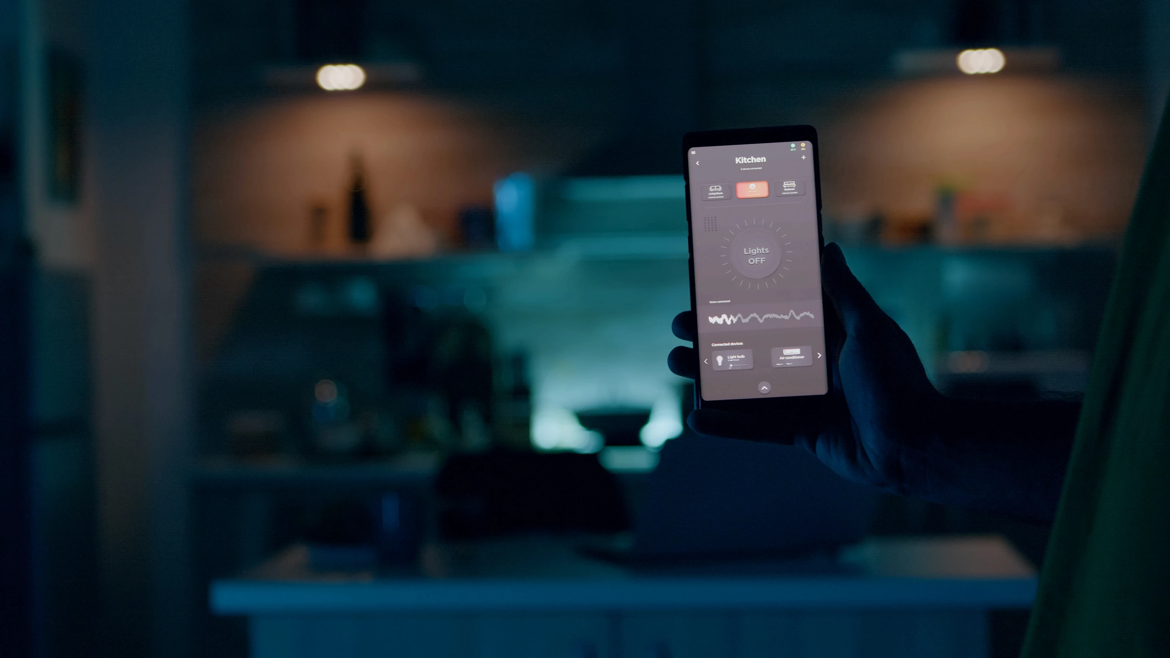 Person holding a smartphone displaying an automation app interface in a dimly lit smart home kitchen.