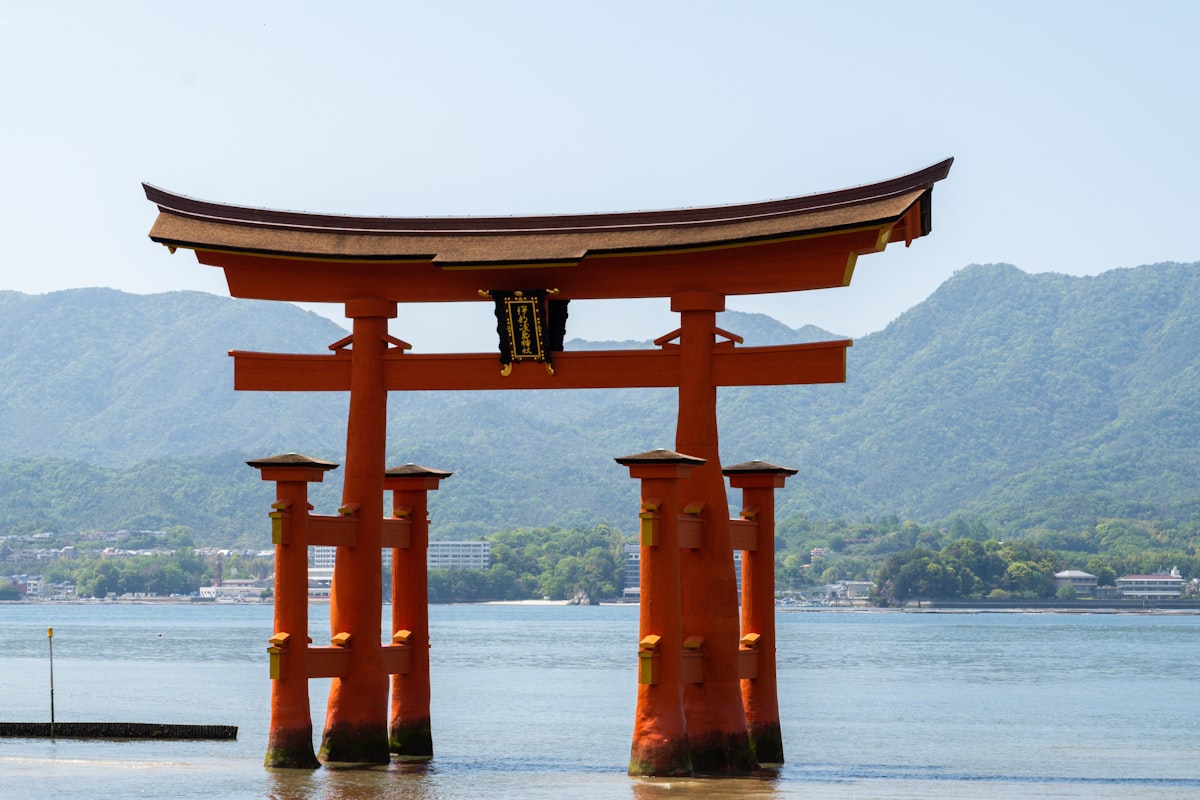 Itsukushima floating torii gate standing in the water at high tide with green mountains behind it