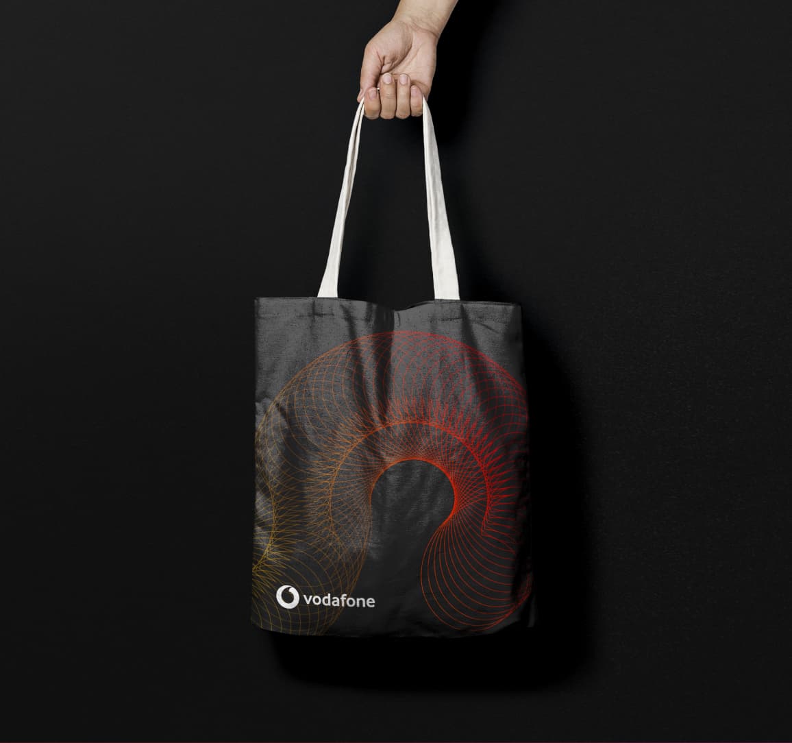 Black tote bag displaying a vibrant orange spiral graphic and the Vodafone logo, designed for internal brand awareness.
