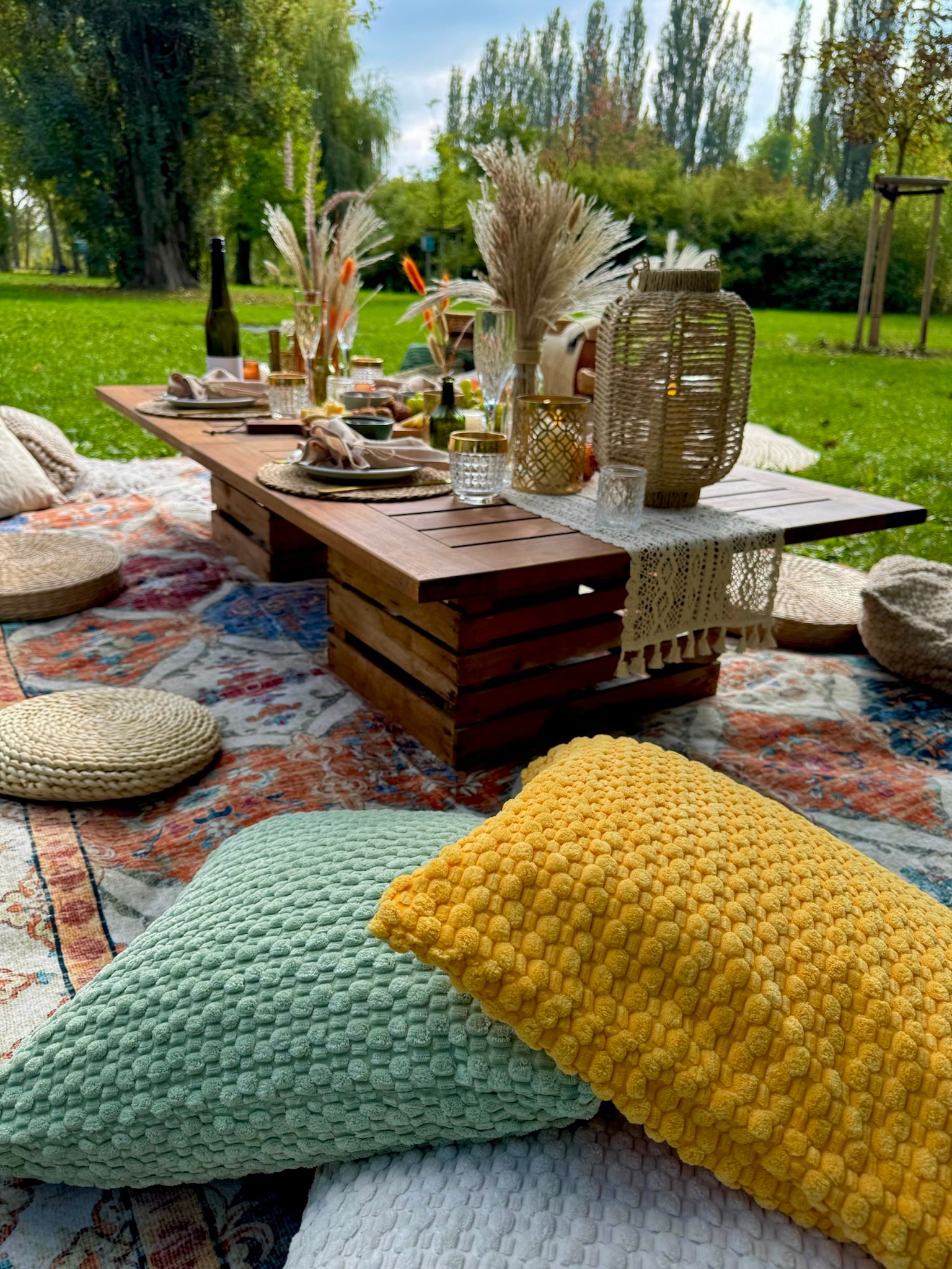 Detailansicht einer Hochzeits-Picknick-Deko im Boho-Stil mit Blumen und Kerzen auf einem Holztisch..