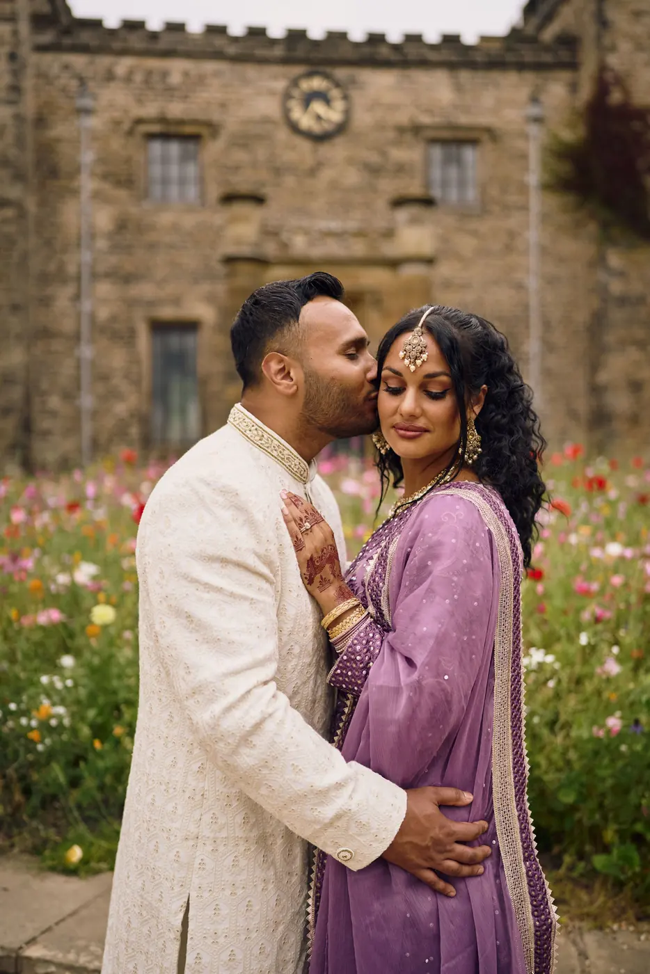 Farhan kissing Demi’s cheek among wildflowers below Towneley Hall’s clock tower