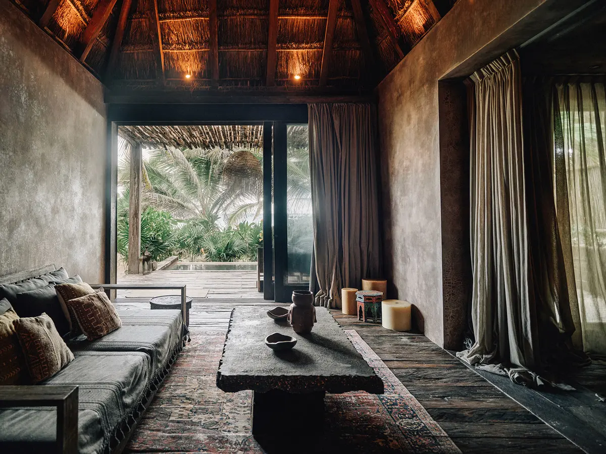 Premier Suite at Nômade Tulum featuring large glass window with view of private pool and palm trees, and comfortable seating area with sofa and center table.