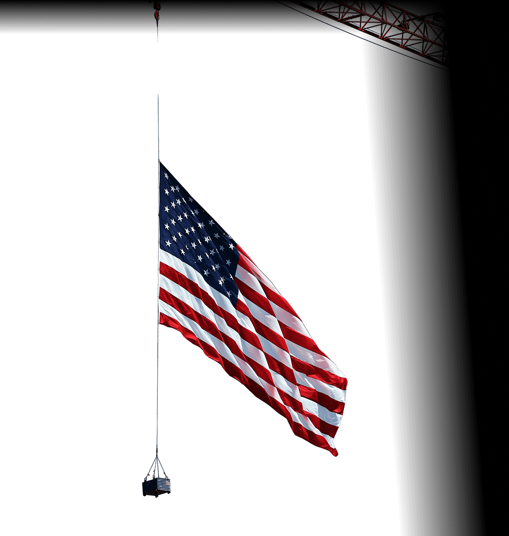 American flag suspended from a crane against a bright sky.