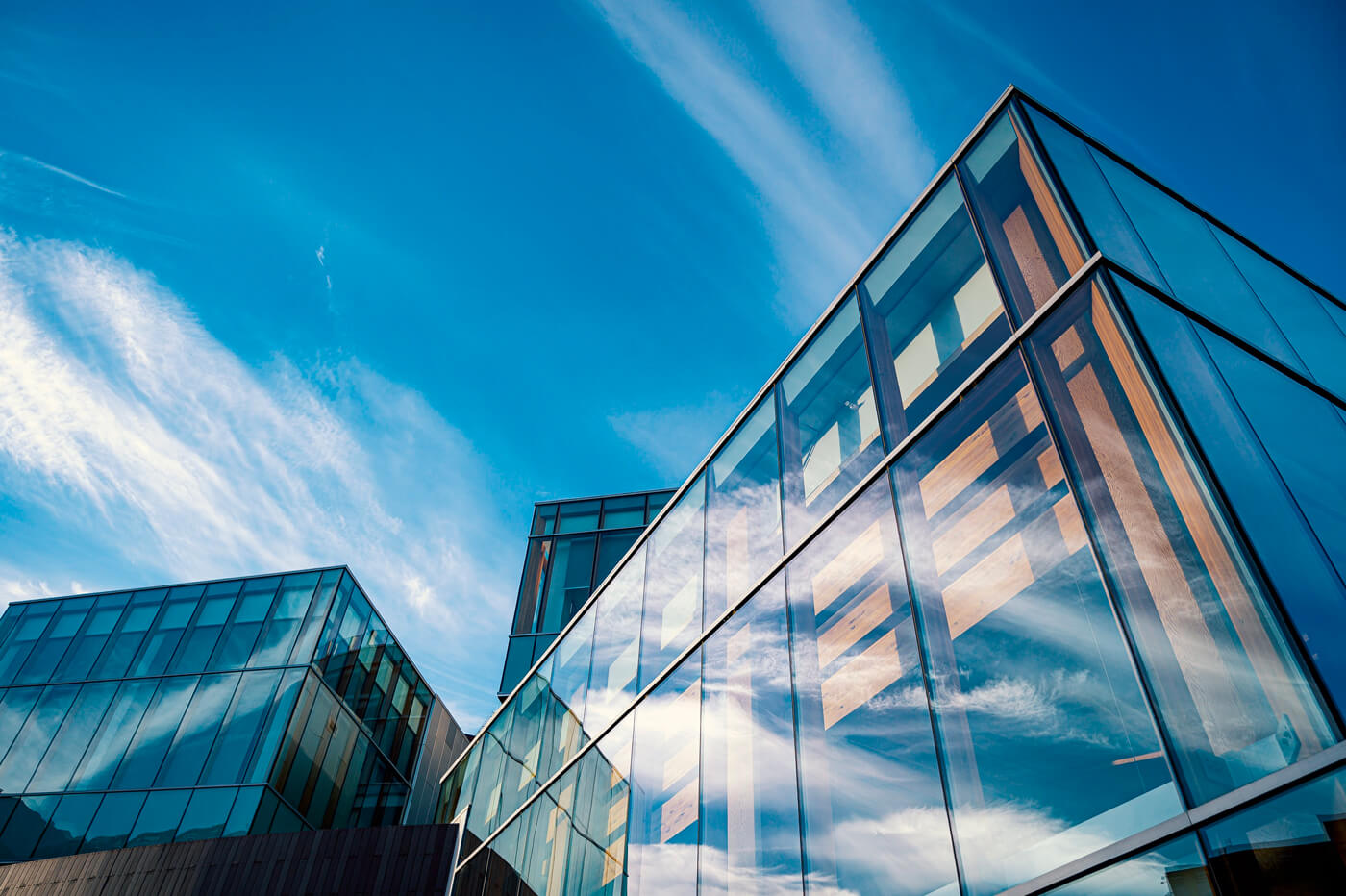 A man in a dark sweater and a woman in glasses wearing a navy blouse sit together at a desk, smiling at the camera with a laptop in front of them.