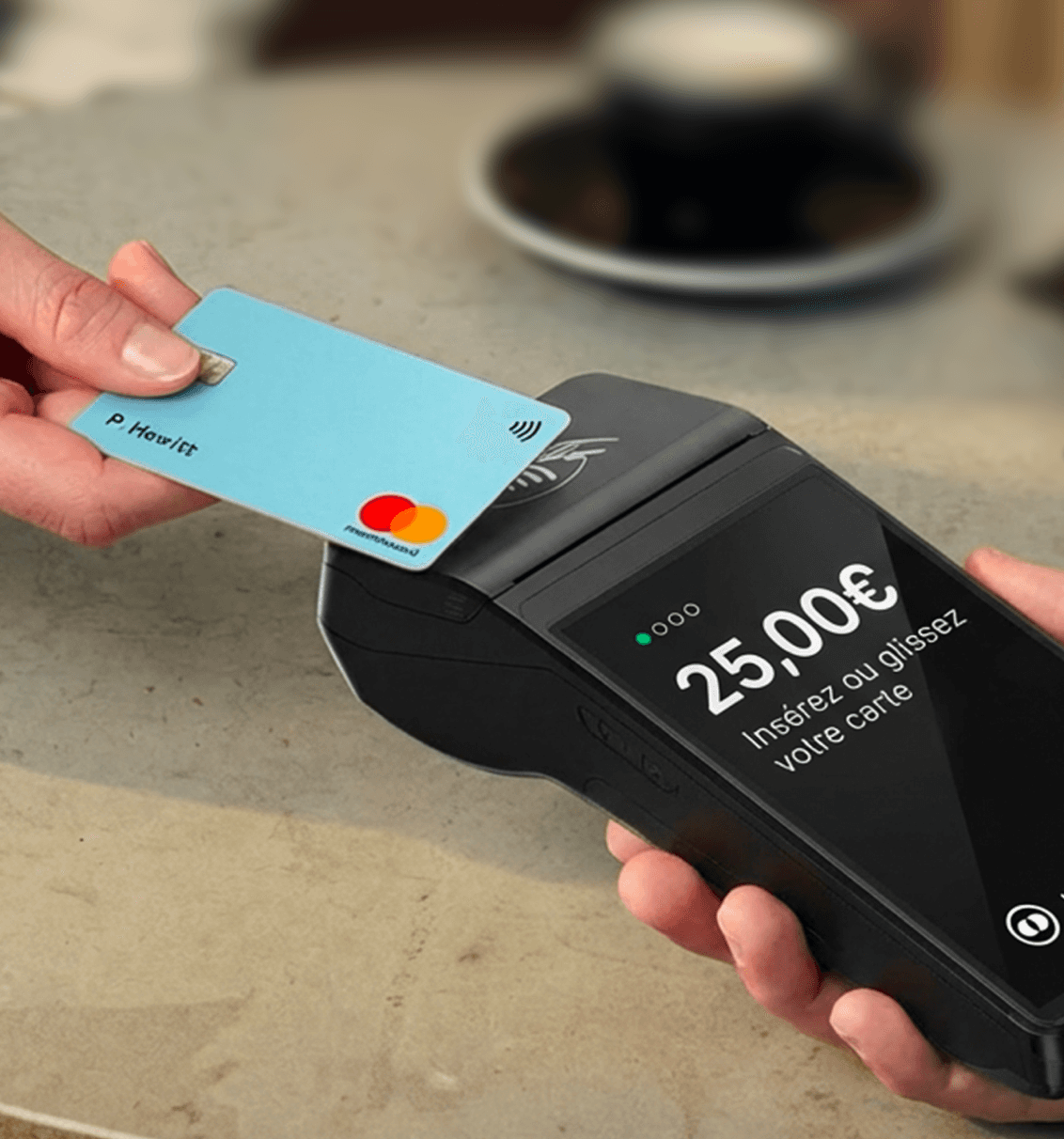 Close-up of a hand holding a card payment terminal showing a €25.00 charge as a blue card is tapped.