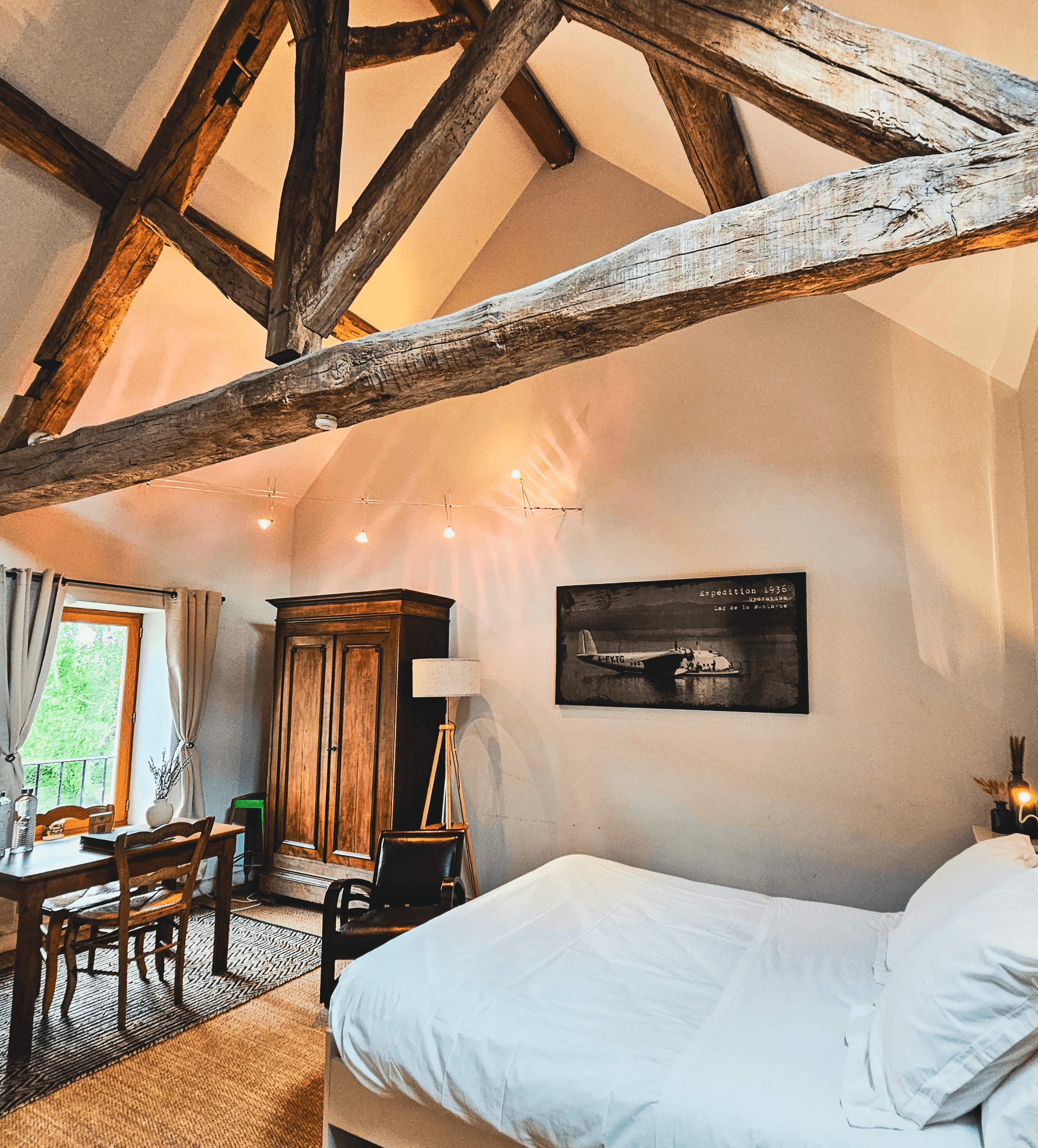 Chambre rustique avec poutres apparentes, lit confortable, armoire en bois et table à manger. Décoration intérieure chaleureuse.