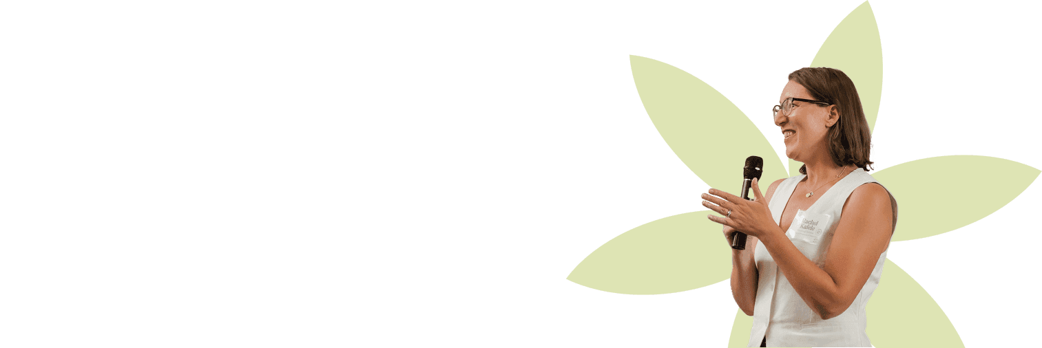 A person wearing a beige collared shirt is giving a speech, holding a microphone with an expressive hand gesture, set against a backdrop featuring a stylized yellow floral design.