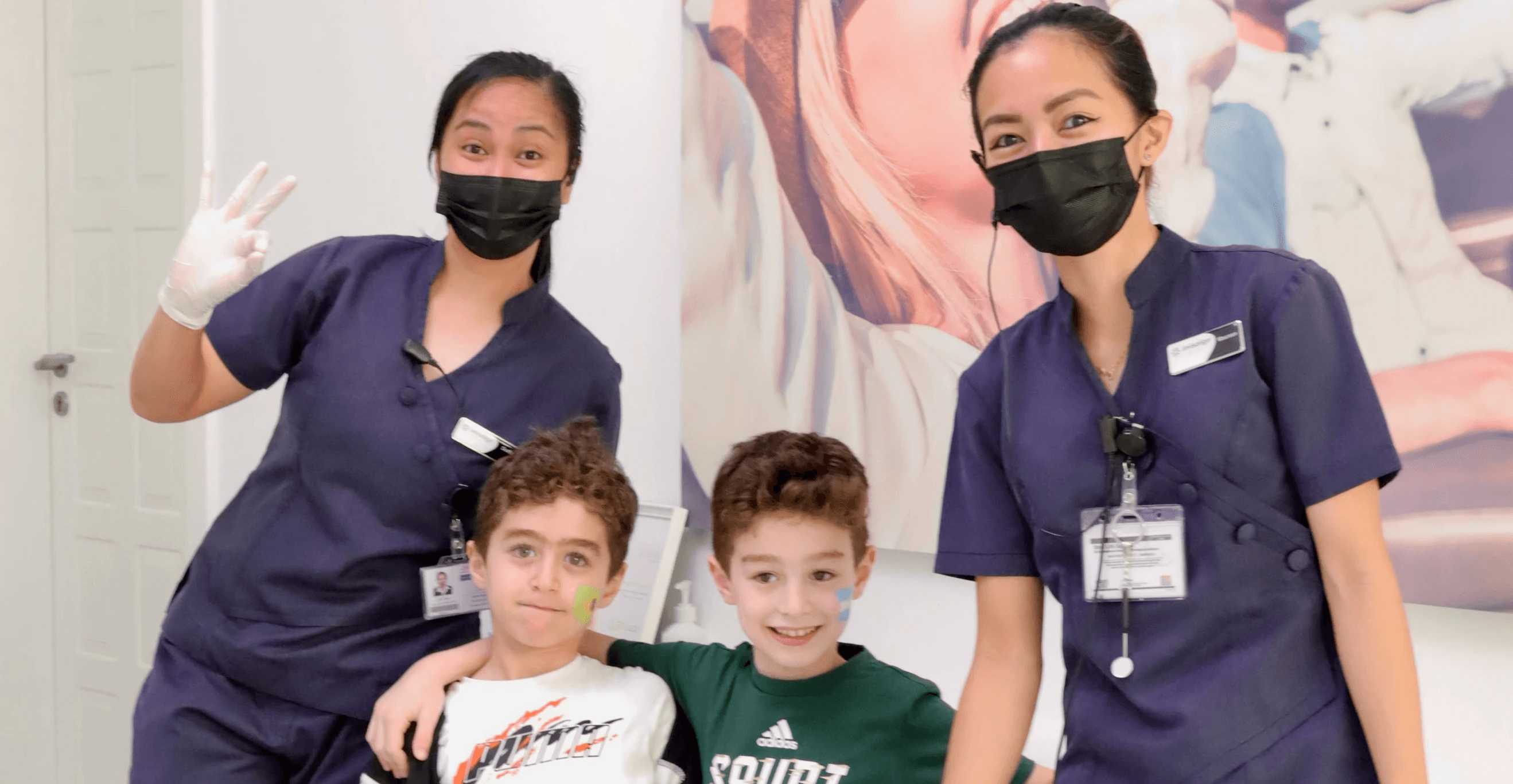 Two kids smiling together with Invisalign Center staff, having their baby teeth checked