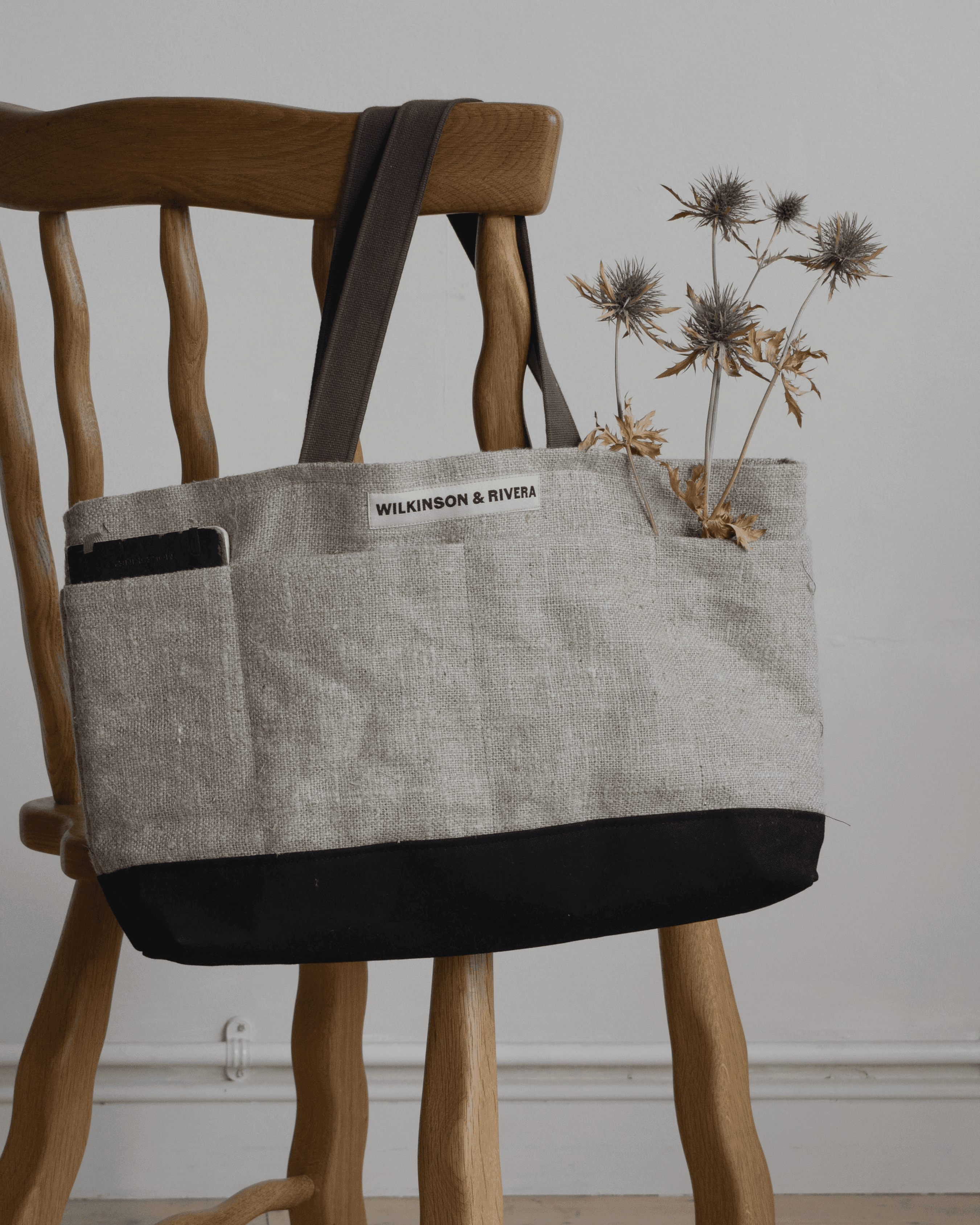 Limited edition Garden Tote from Wilkinson & Rivera in Raw Linen hanging from chair with a notebook in one pocket and flowers in another