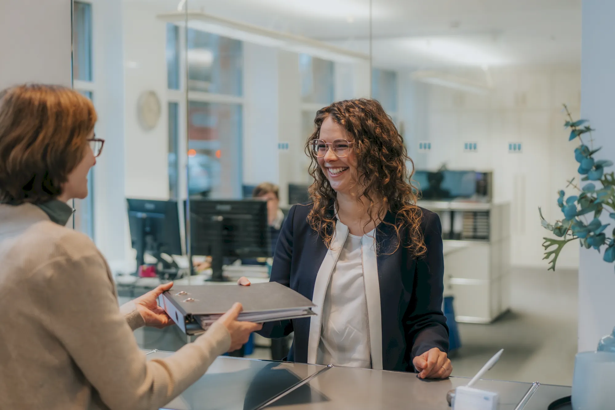 Büroarbeit: Angestellte übergibt Aktenordner an lächelnde Kollegin am Empfang. Büroalltag.