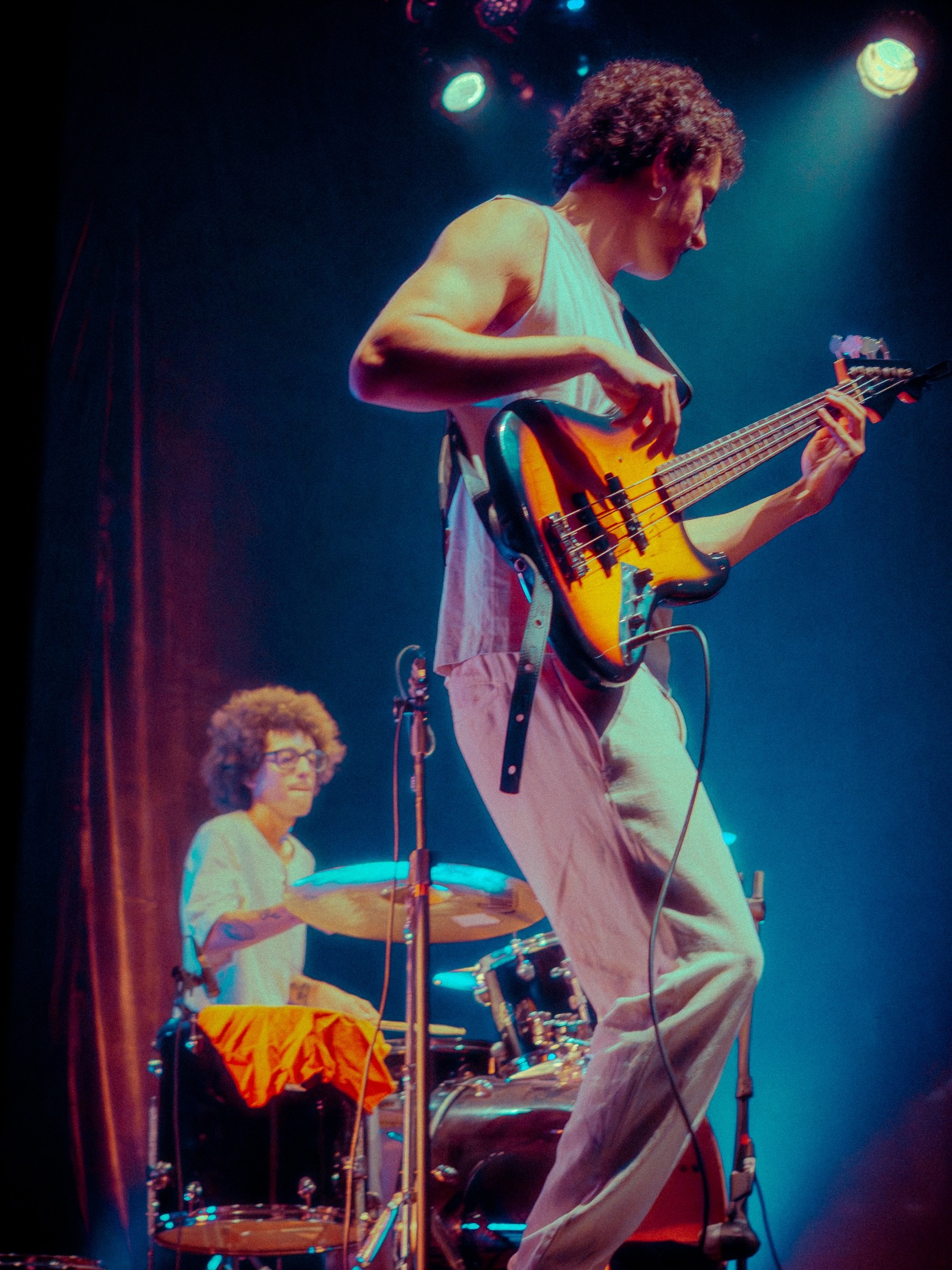 Live event photography of two musicians, a drummer and a bass player, performing on a stage