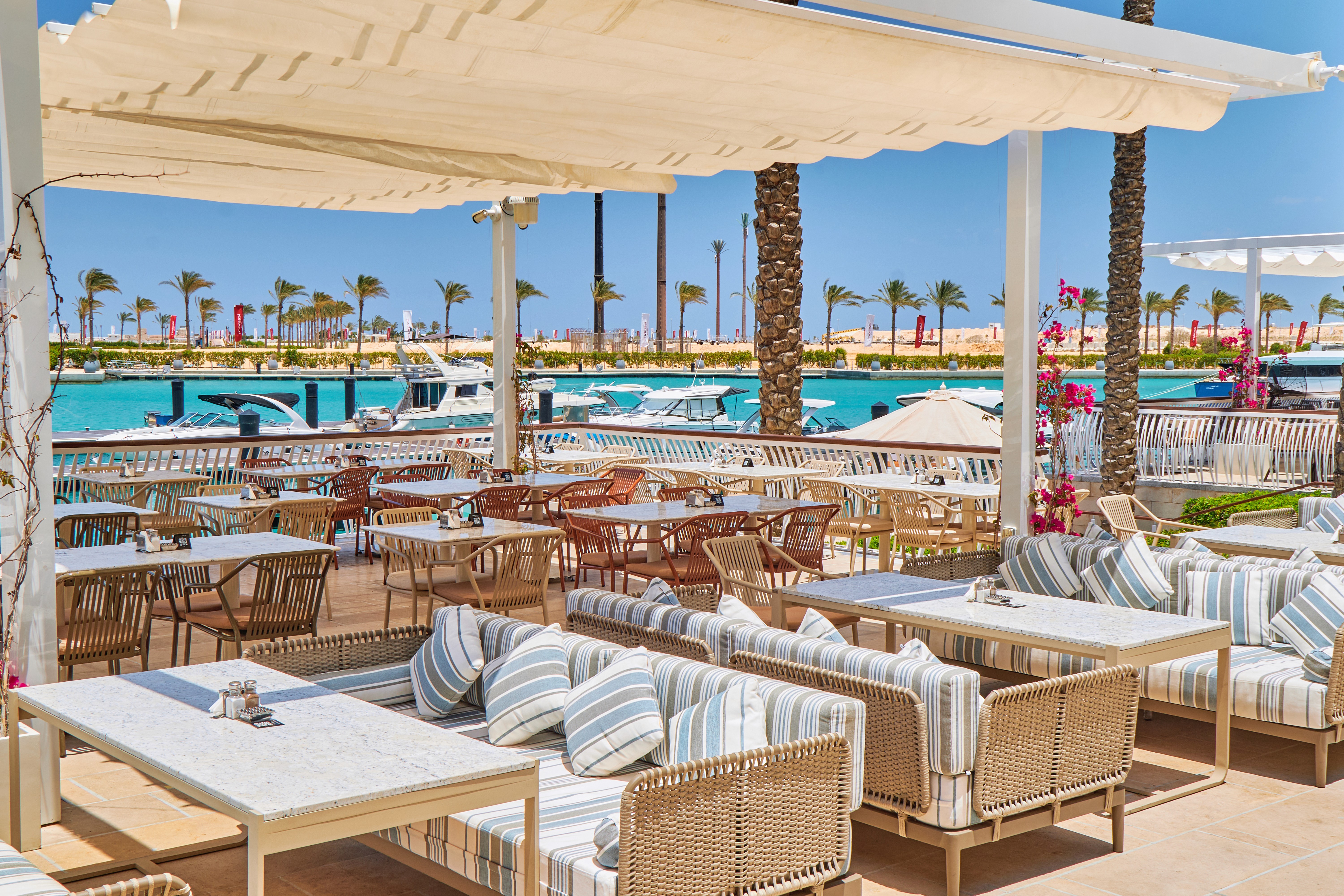 An overhead shot of a large oval plate featuring sliced, roasted duck, half glazed with a sauce, served over two thin pancakes and alongside steamed bok choy, surrounded by small bowls of condiments like scallions, sauce, salt, and carrot shreds.