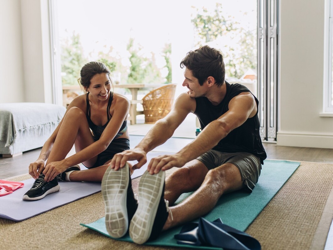 couple smiling at one another as they prepare to do their workouts to lose weight at home together in their sunny living room