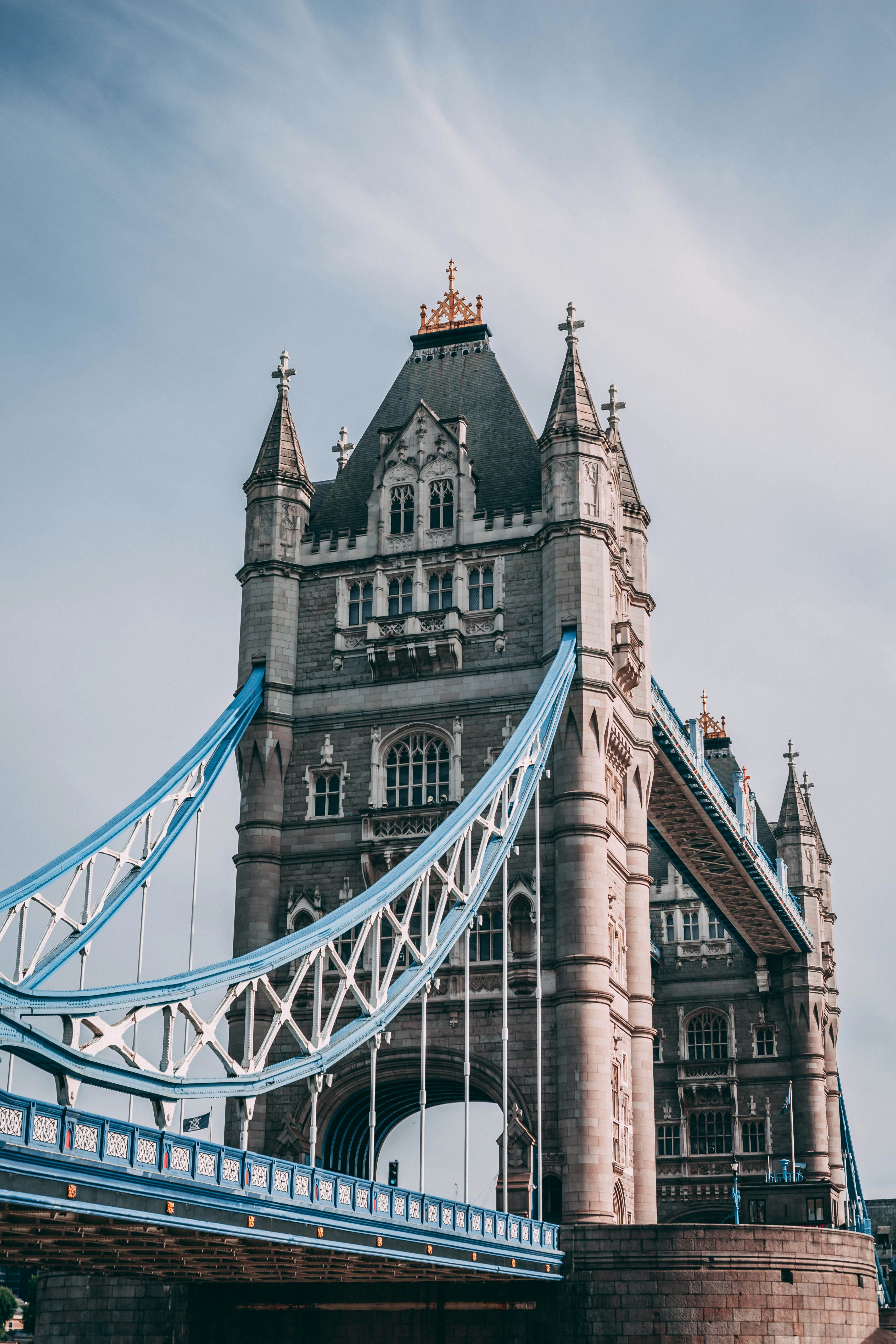 One of the gray stoned towers of the Tower Bridge in London, with blue suspension cables spanning from the sides. 