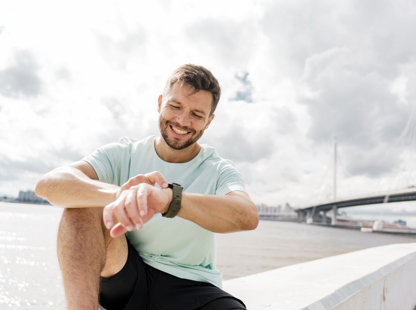 man checking his fitness watch while sitting outside to see how far to run to lose weight he still has to go