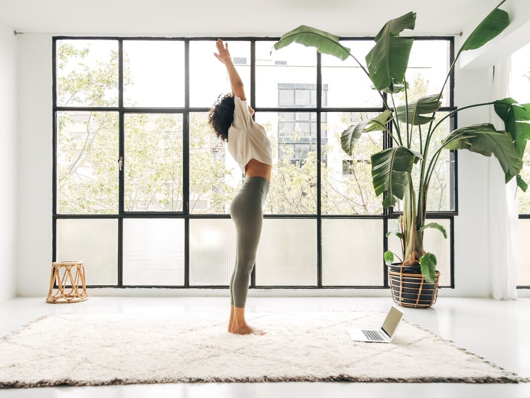 woman using her laptop to follow yoga asanas for weight loss as she does sun salutations