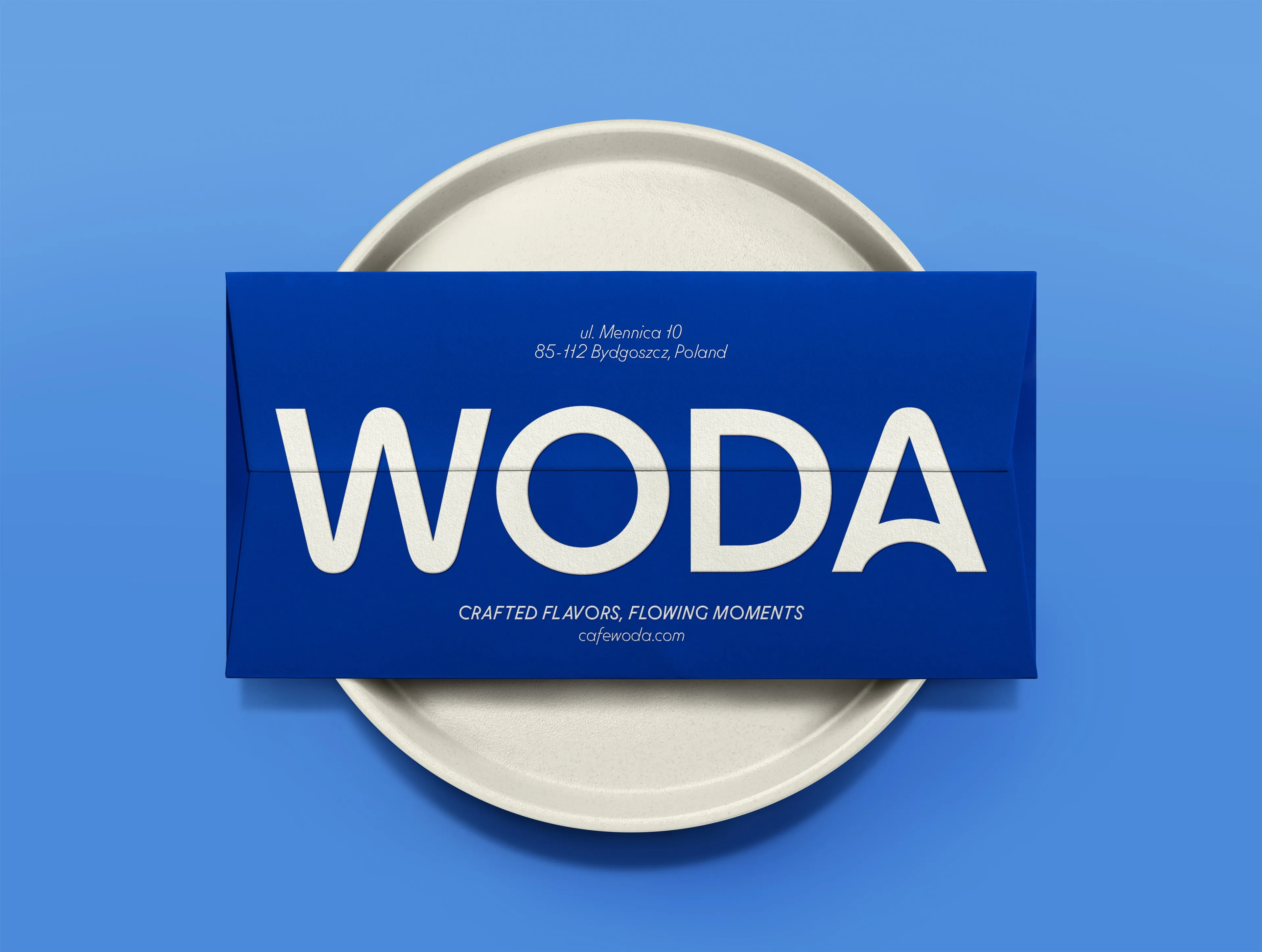 Blue Woda envelope with cream logotype on a ceramic plate, restaurant stationery and brand identity design