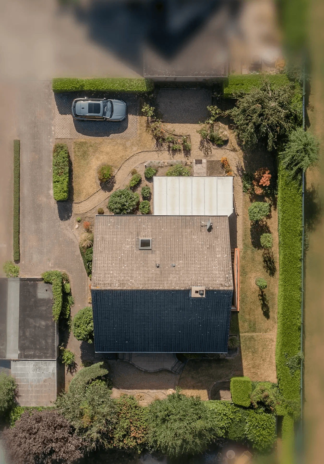 Senkrechte Luftaufnahme des Hauses mit Wintergarten und Garten; die Umgebung ist weichgezeichnet.
